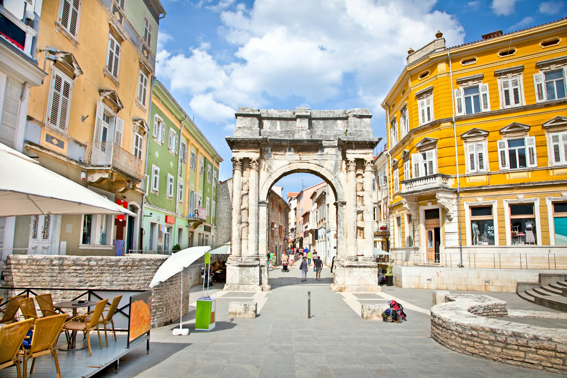 People walk near the Sergius Arch in Pula on a sunny day