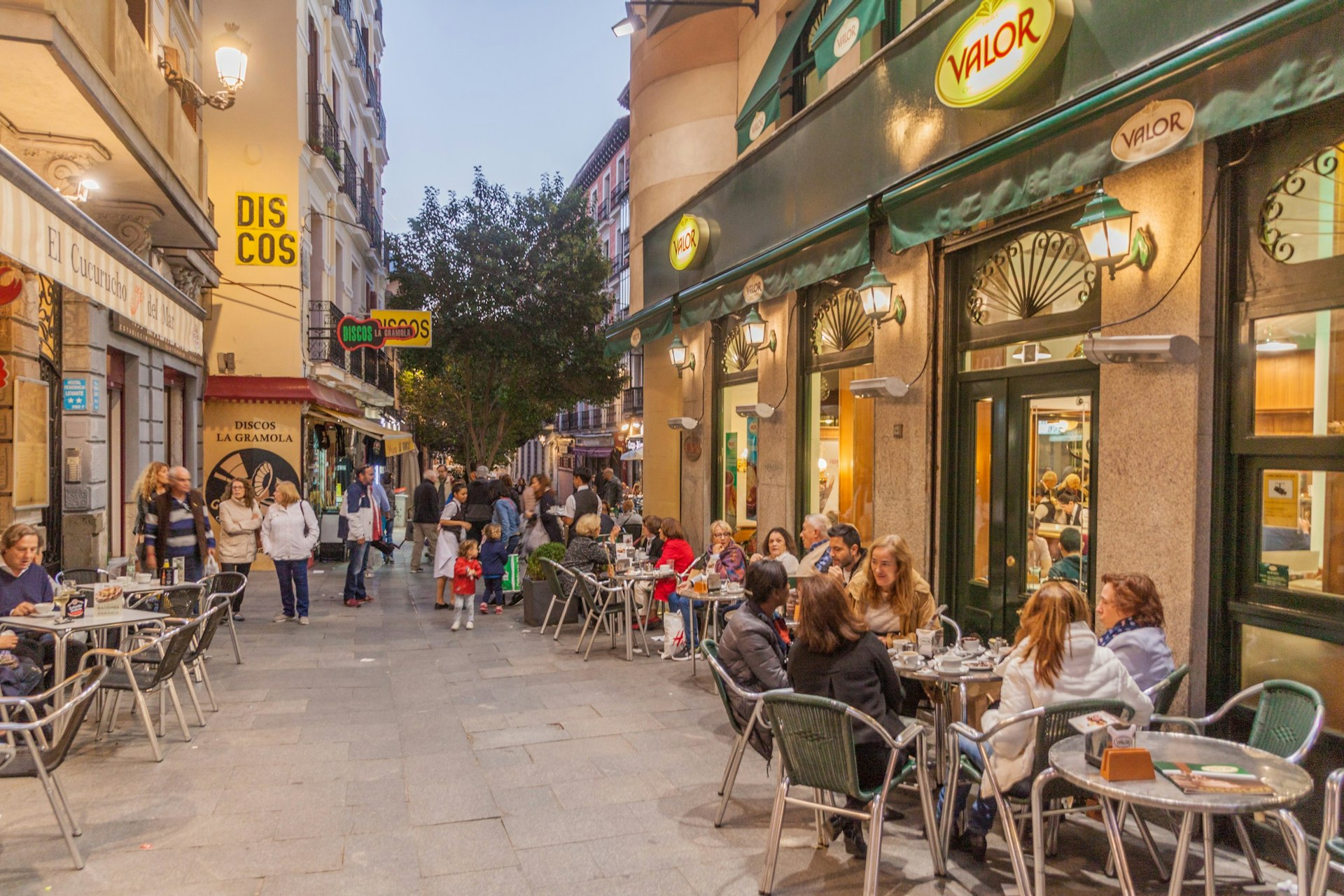 Street cafes lively with people sitting and dining at restaurant terraces in the center of Madrid.