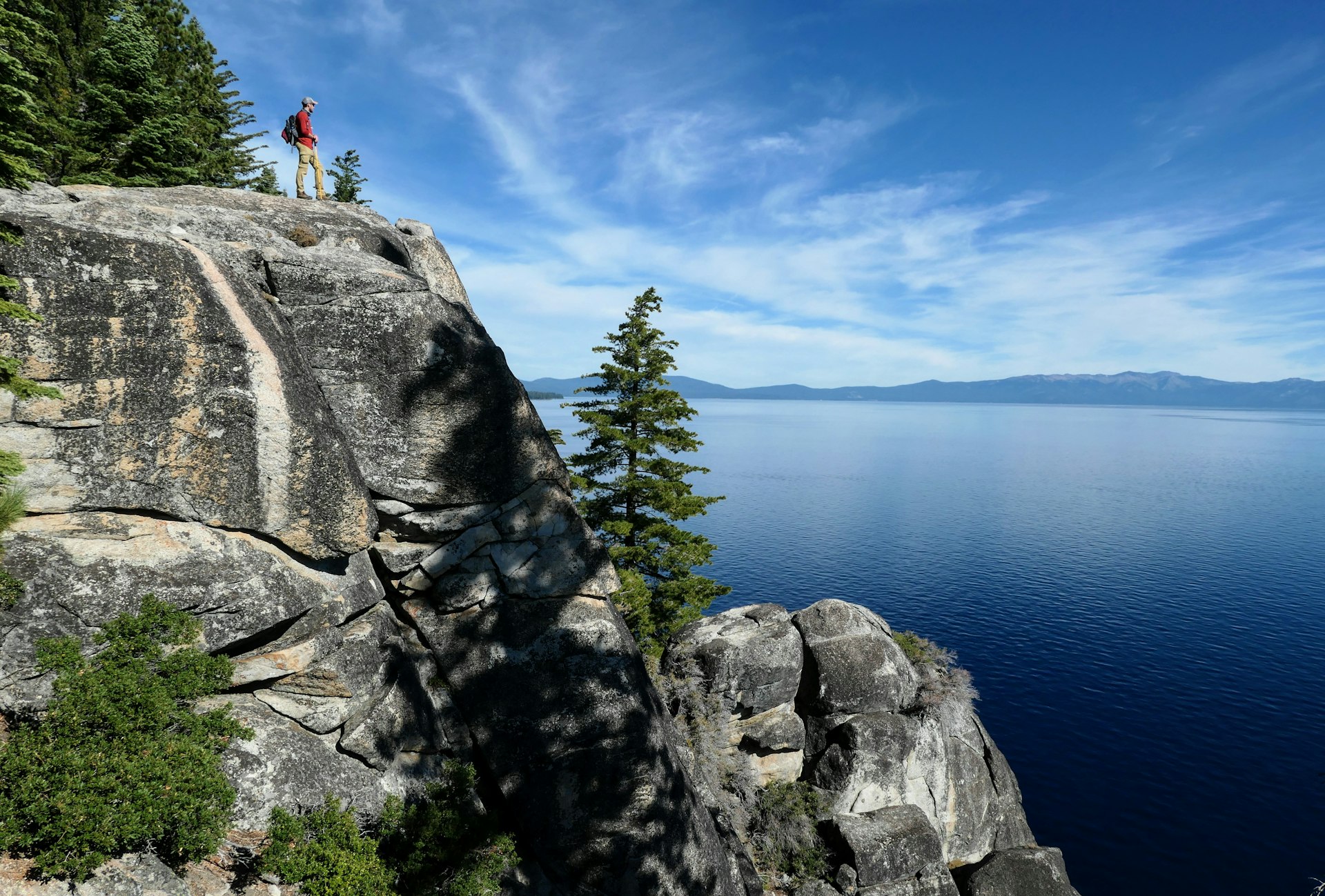 A hiker stands on a rock looking out over beautiful lakeside scenery