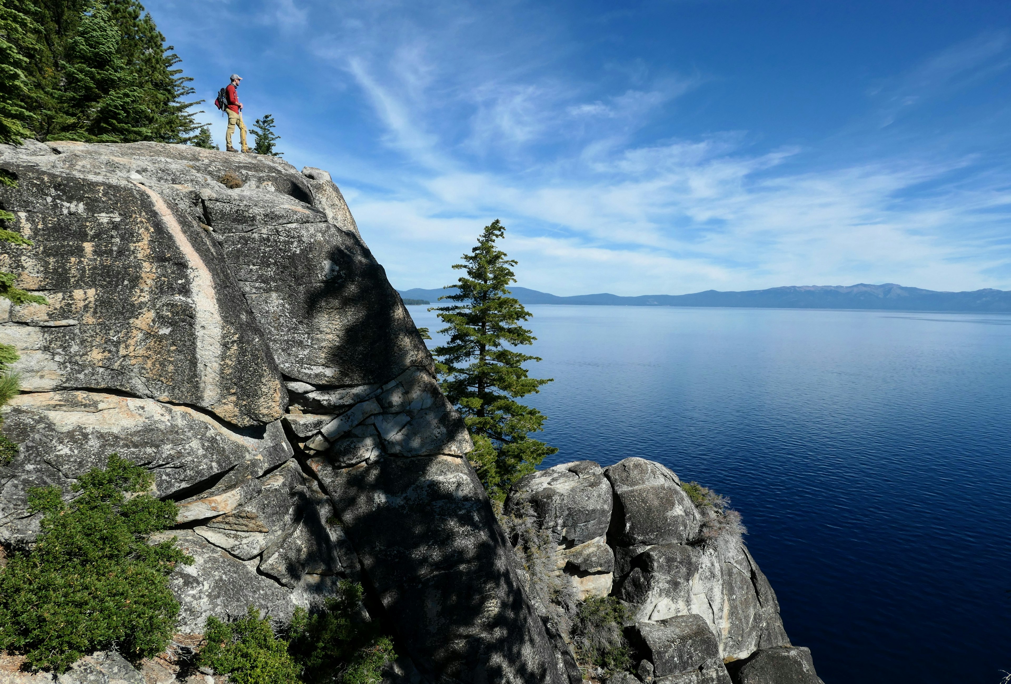 A hiker stands on a rock looking out over beautiful lakeside scenery