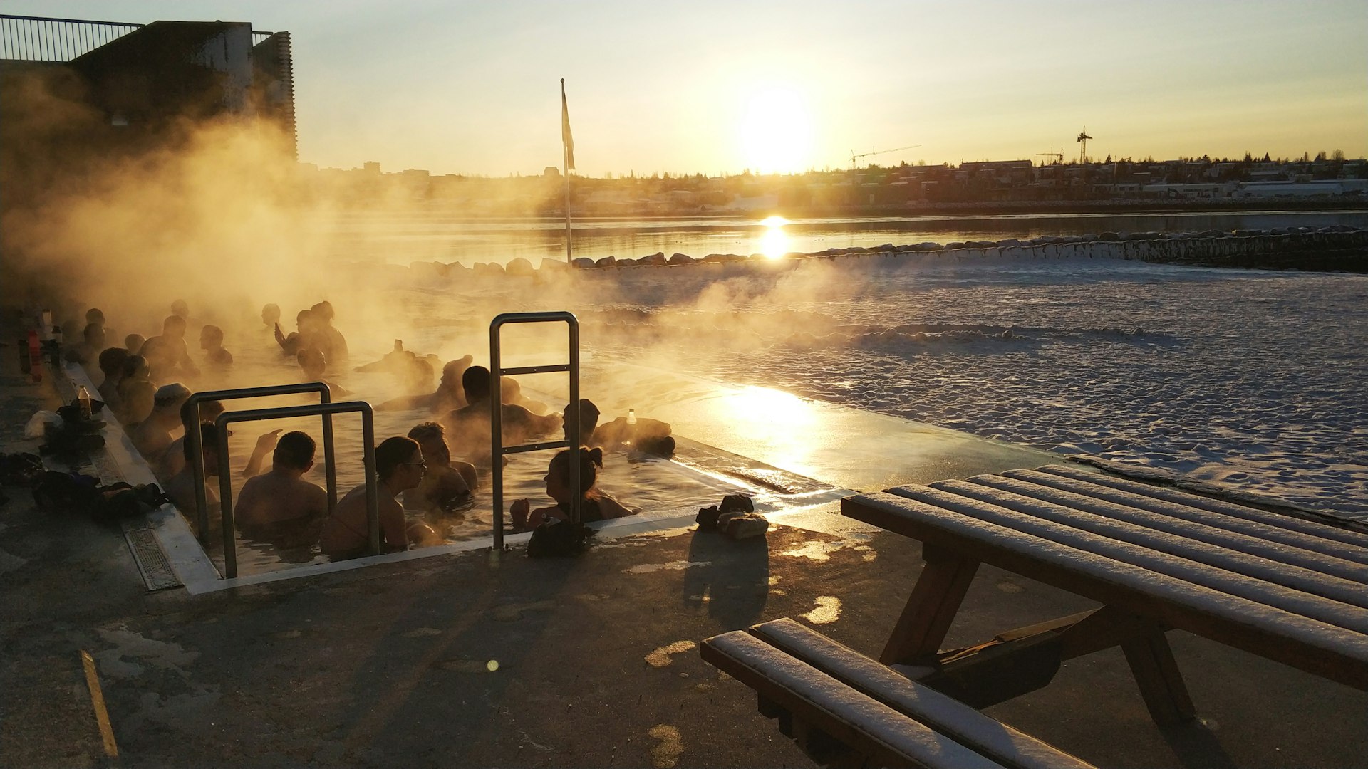 People crowded into a hot tub on a snowy day as the sun sets