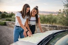 Two women smile and look at a map resting on their car in Italy