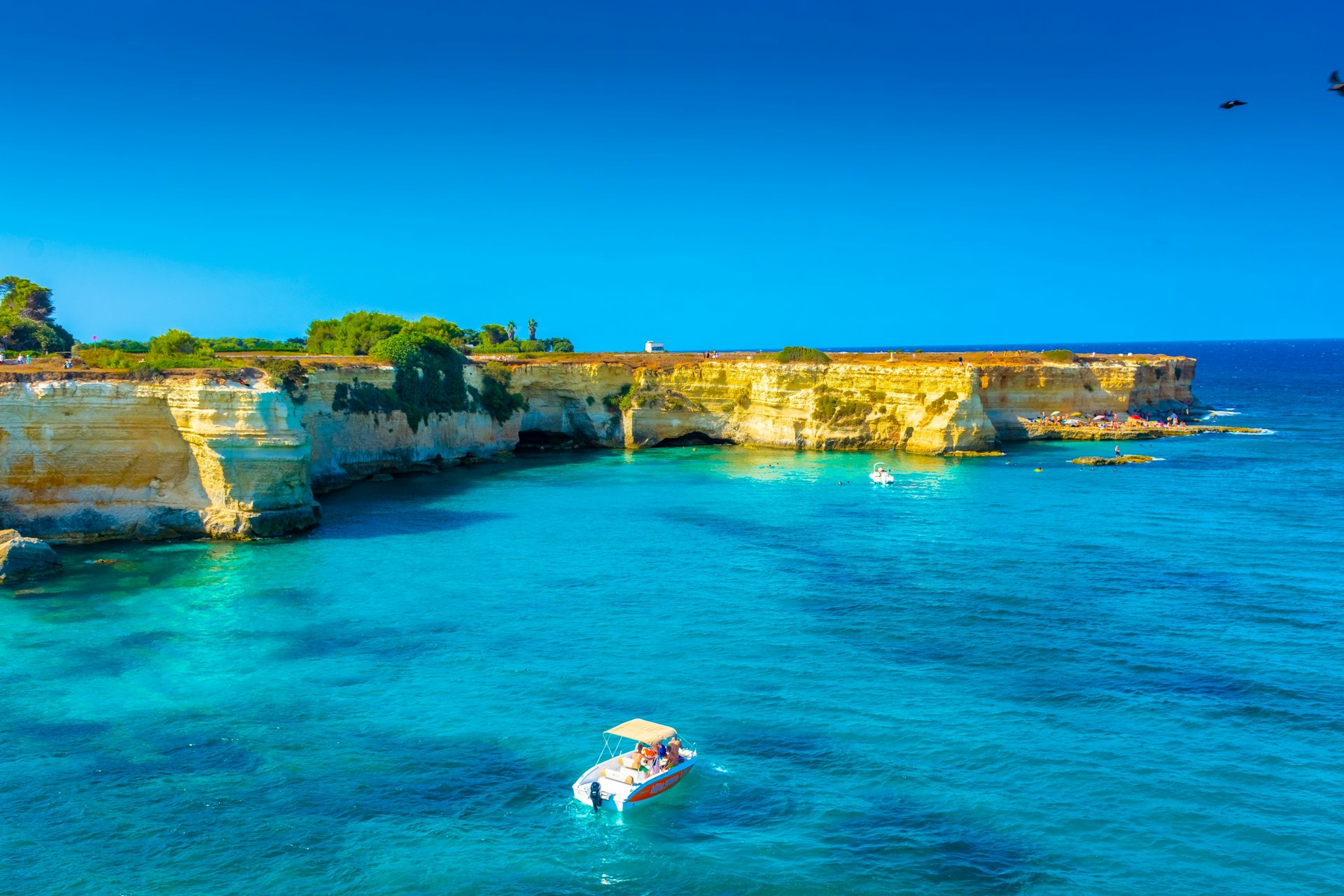 A boat sails by rocky cliffs in the waters off Torre Sant’Andrea, Puglia, Italy