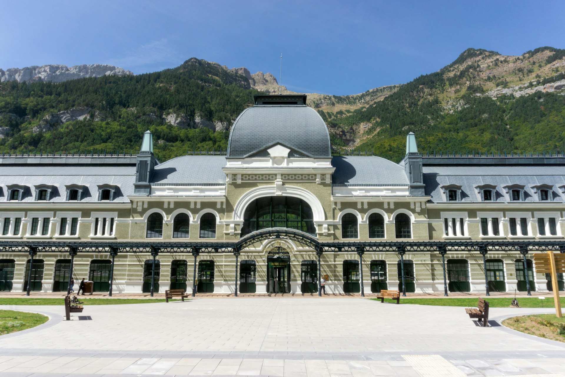 The exterior of a large train station building backed by mountains