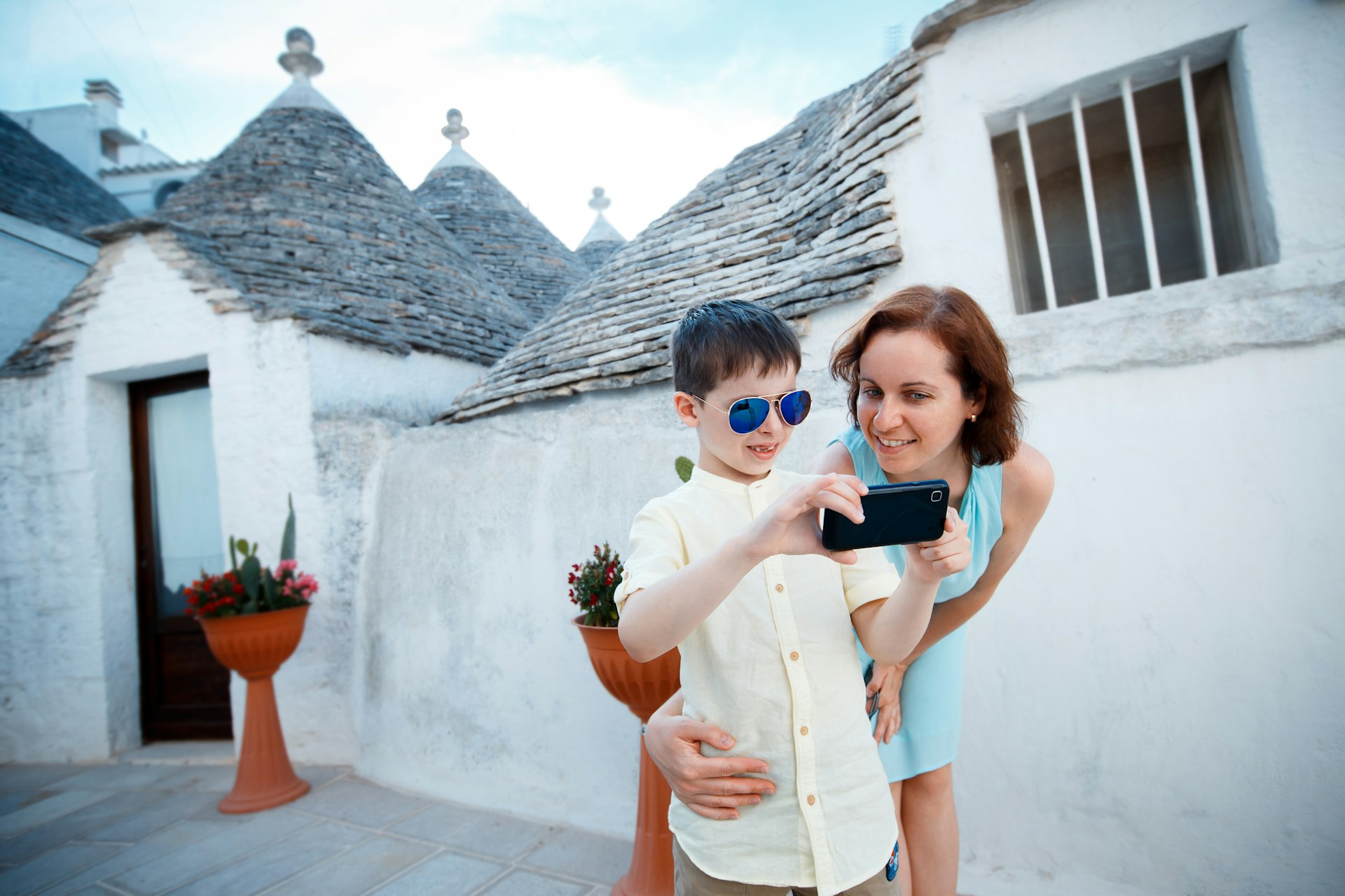 A mother and son pose for a photograph in a town with lots of low-rise round white-stone buildings