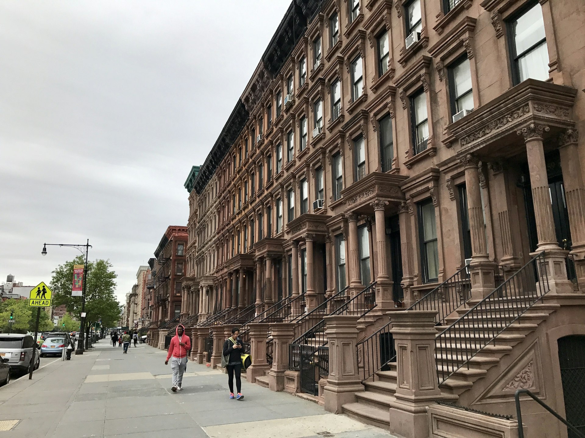 People walk by elegant brownstones on Lenox Ave, Harlem, New York City, New York, USA
