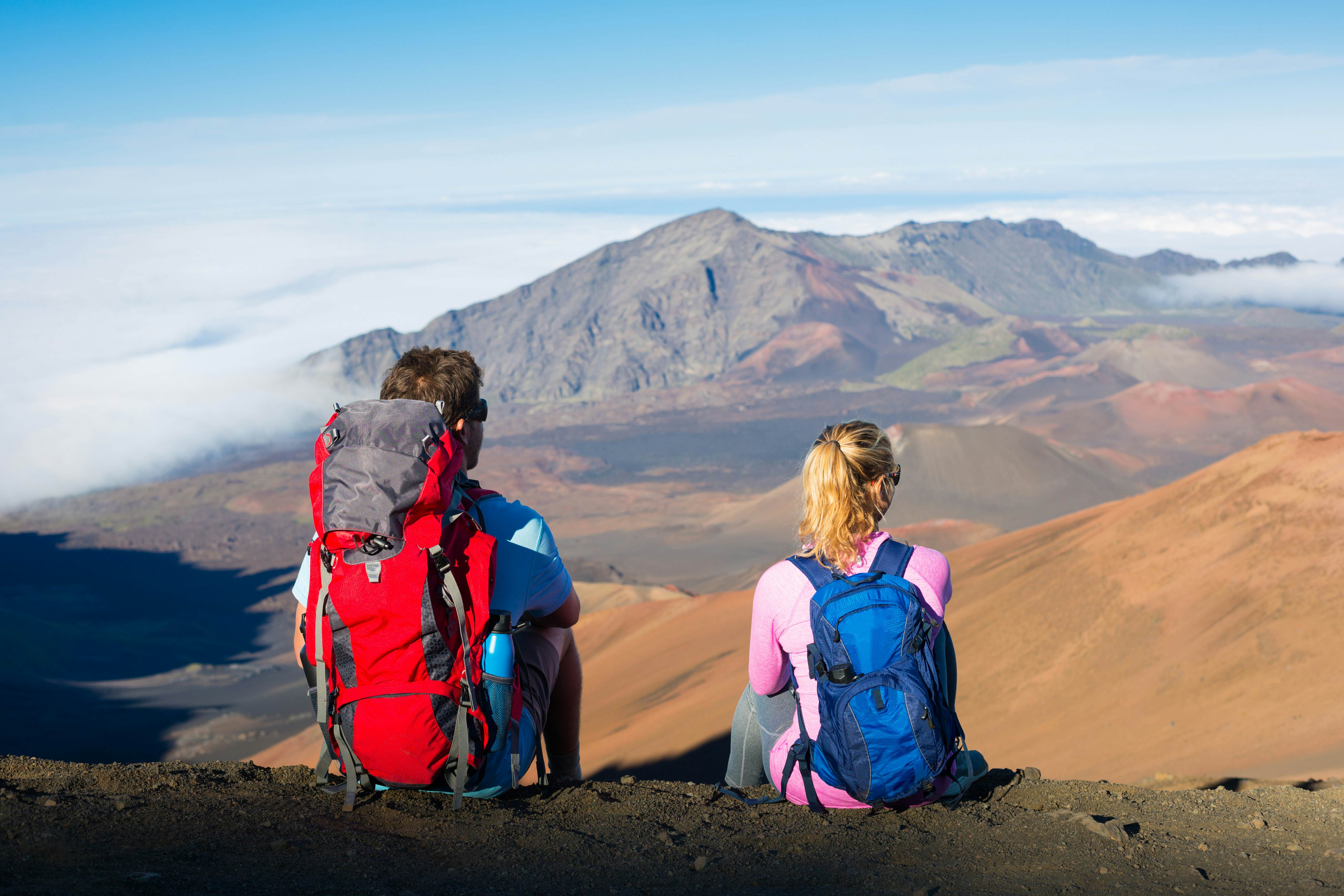 Two hikers with backpacks sitting on the edge of a path looking at the Haleakalā Crater in Maui