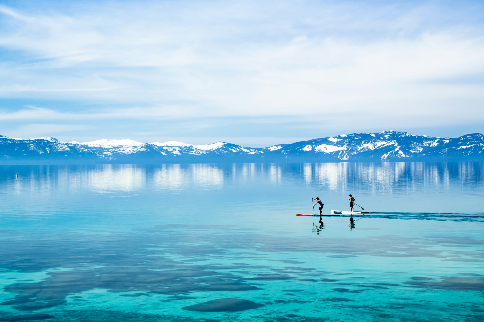 Paddleboarders float out on an alpine lake as the sun shines