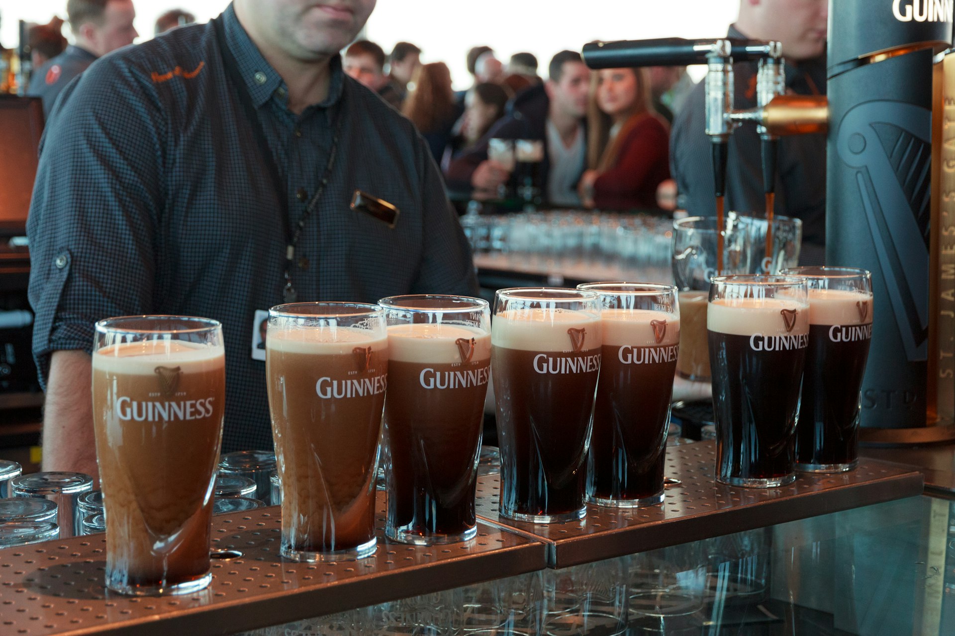 Several pints of Guinness lined up along a bar, at various stages of “settling“