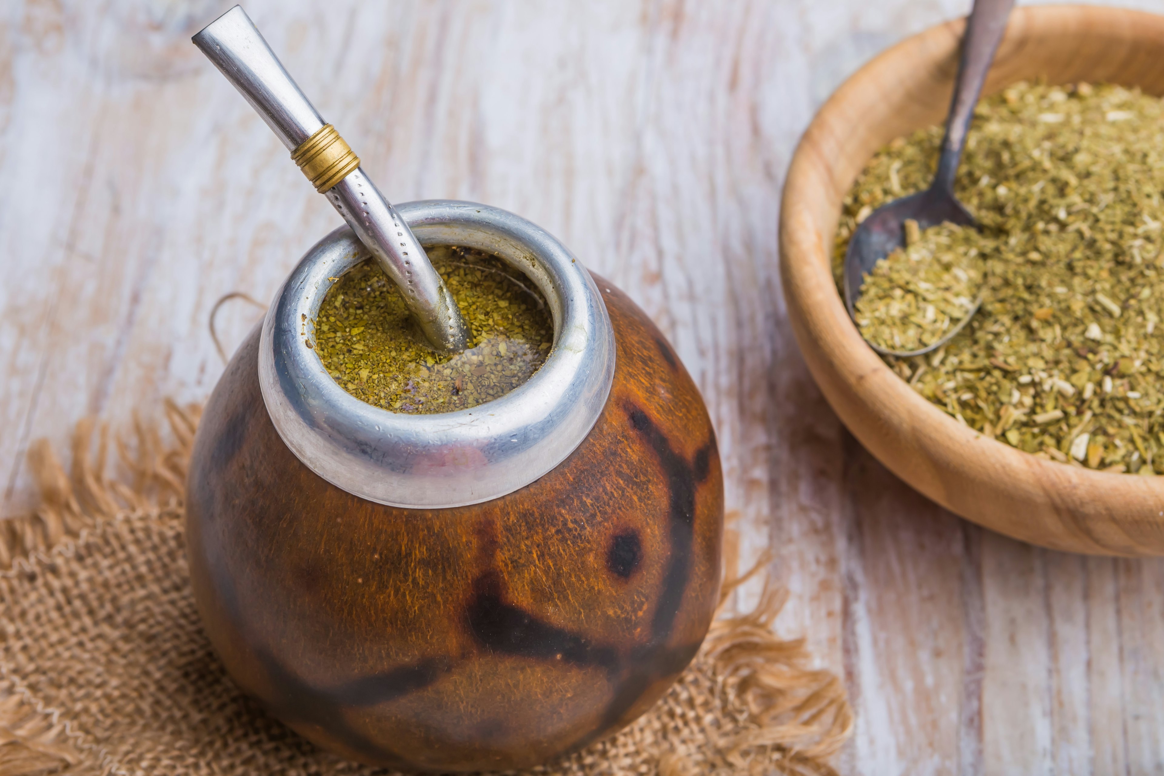 A drink, with a lot of leaves settled on the surface, served with a metal straw