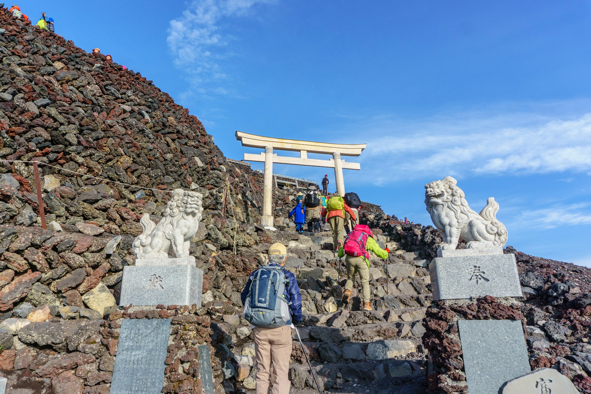 A group of hikers head up a steep series of steps with a torii gate ahead of them