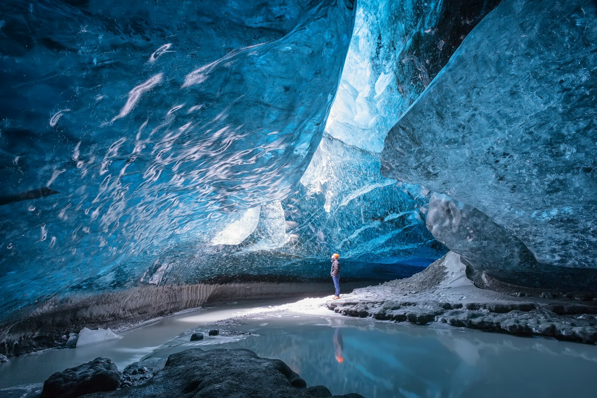 Um homem usando capacete está em uma caverna de gelo olhando para a estranha luz que o rodeia