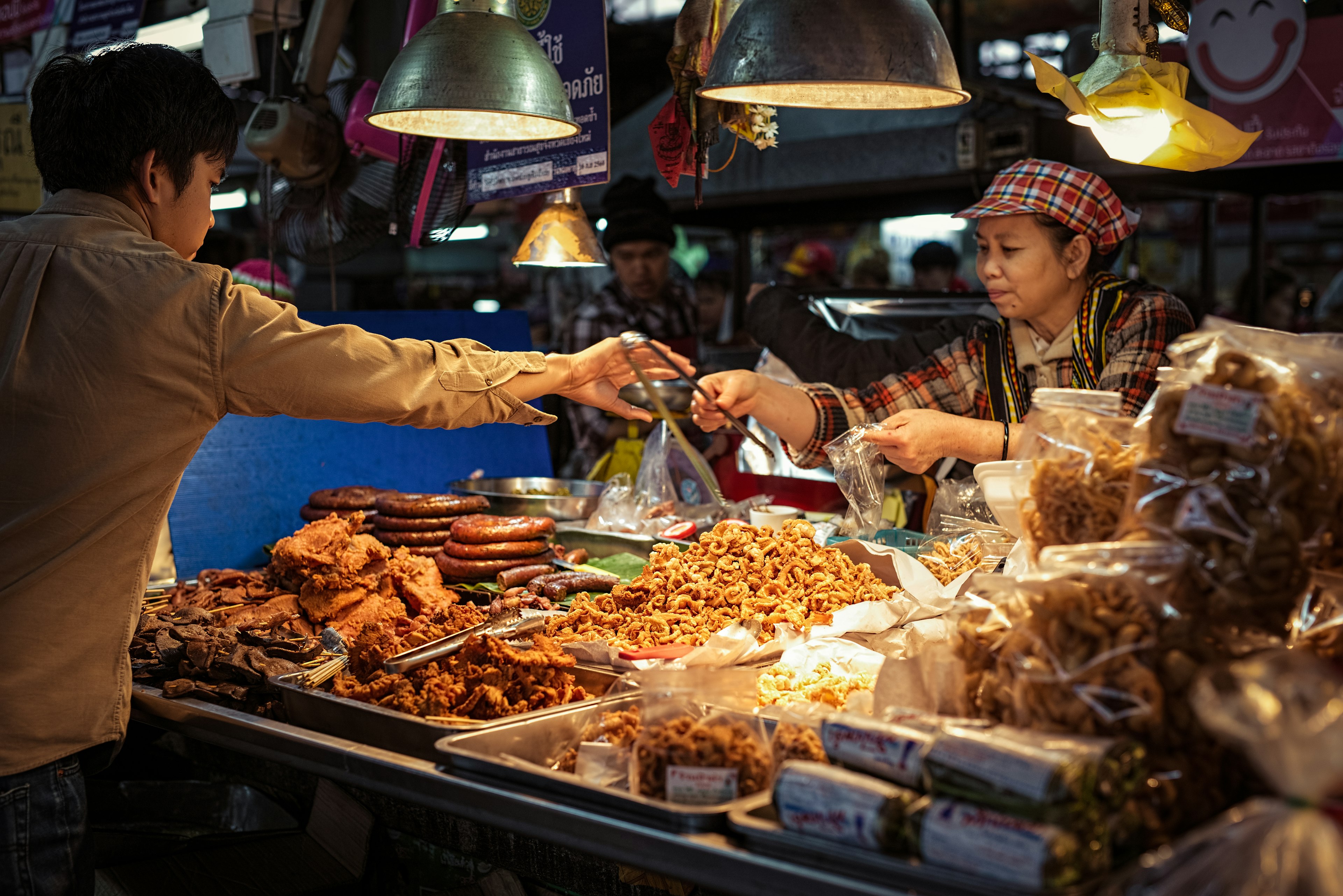 A woman running a food stall hands tongs to a customer so he can select his items