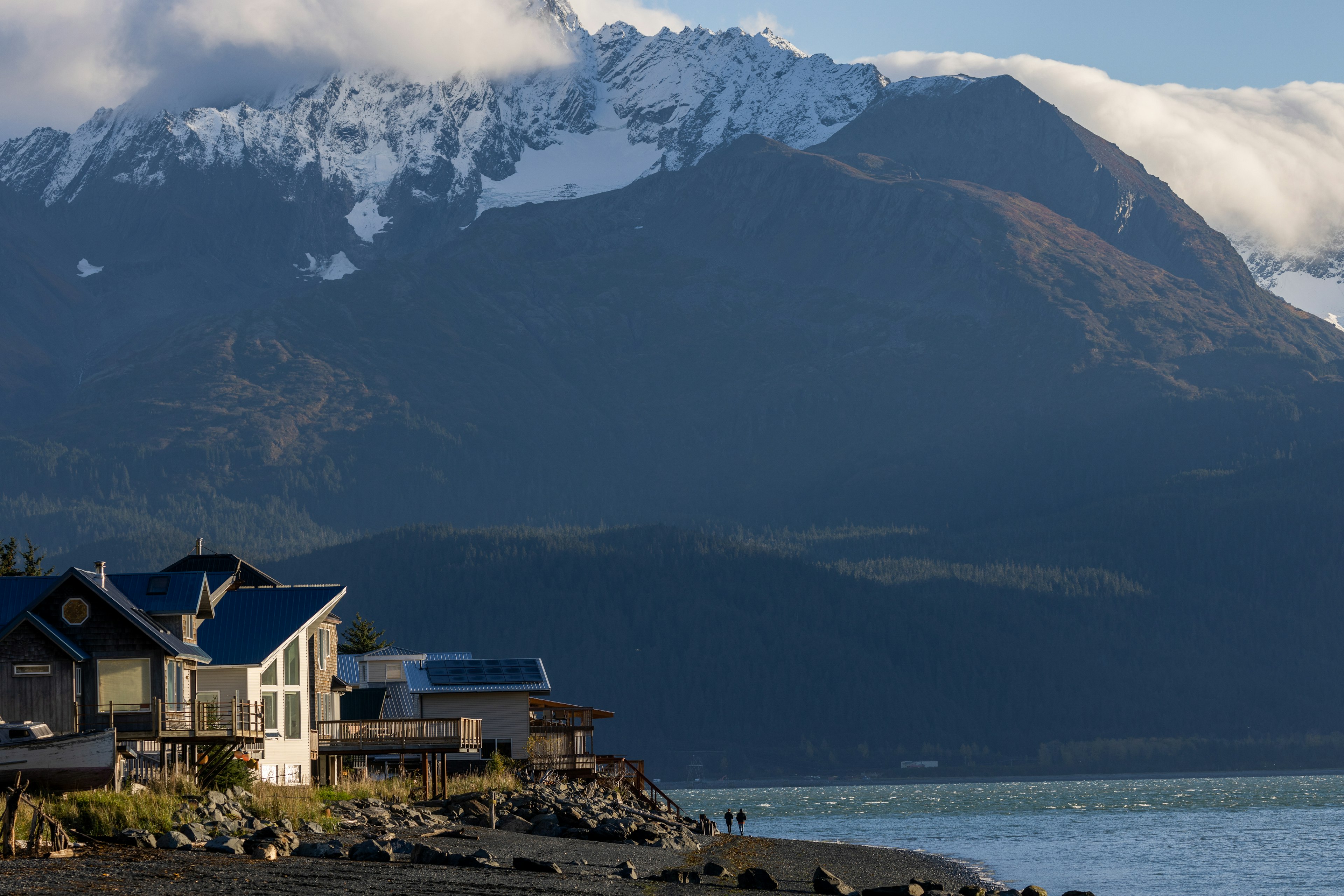 Two people walk in the coastline, their shadows dwarfed by the mountains stretching above them