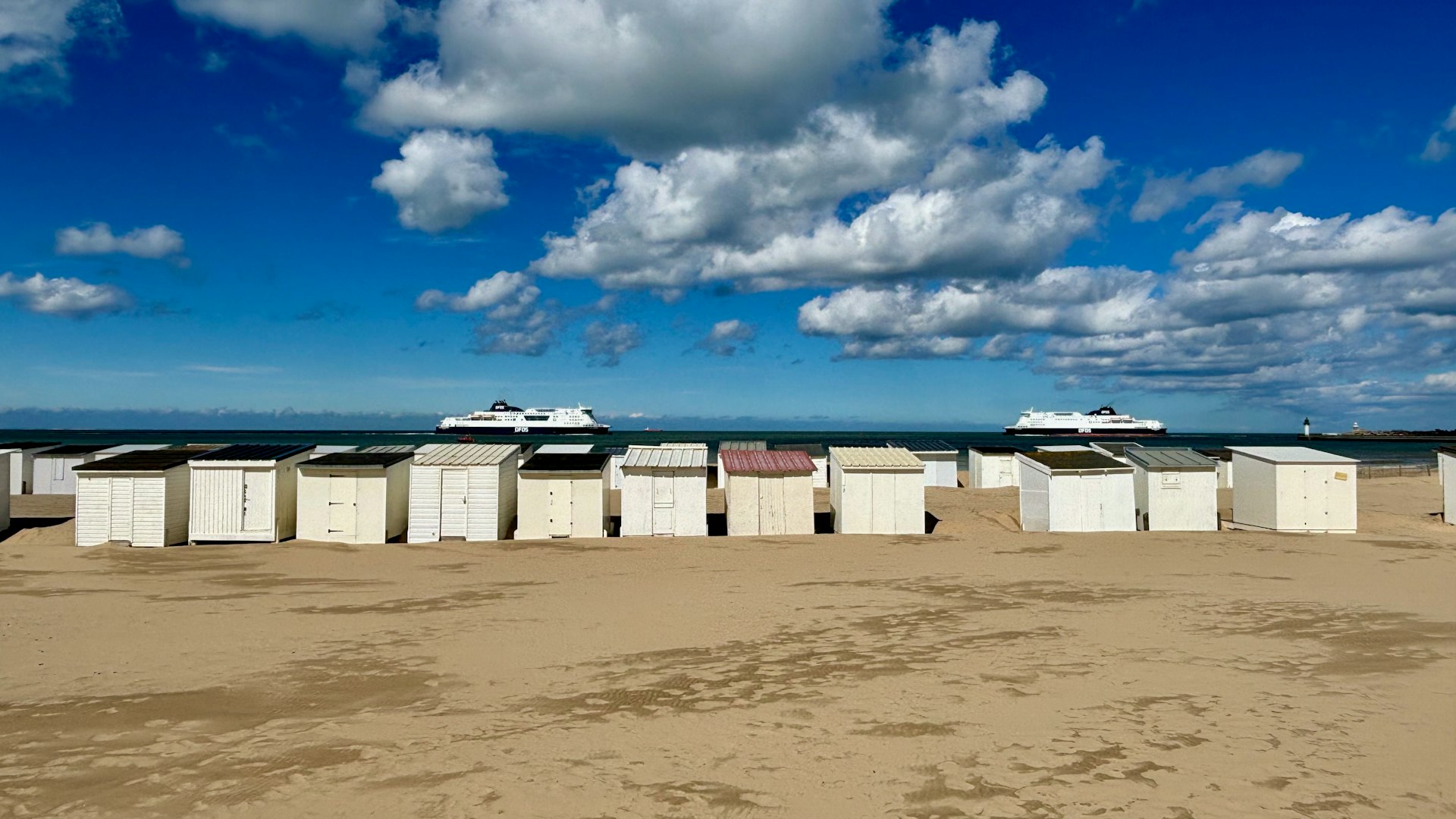 Two ferries out at sea with a row of beach huts in the foreground