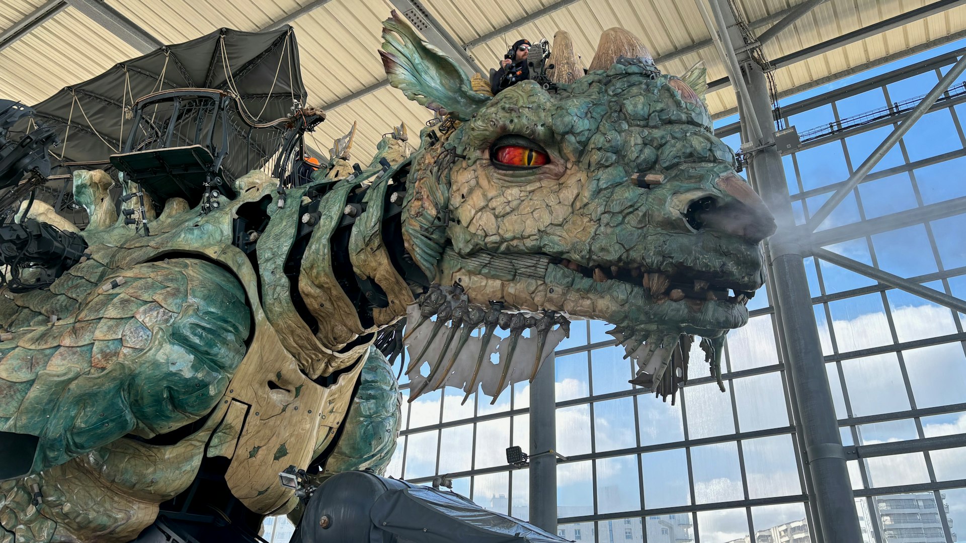 A huge mechanical dragon, controlled by a pilot using levels and pedals, sits in its transparent hangar