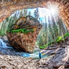 Hiker stands in awe of waterfall and limestone bedrock at a hidden cave in Johnston Canyon at Banff National Park, with sun bursting through the lush forest in the Canadian Rockies.
1015589466