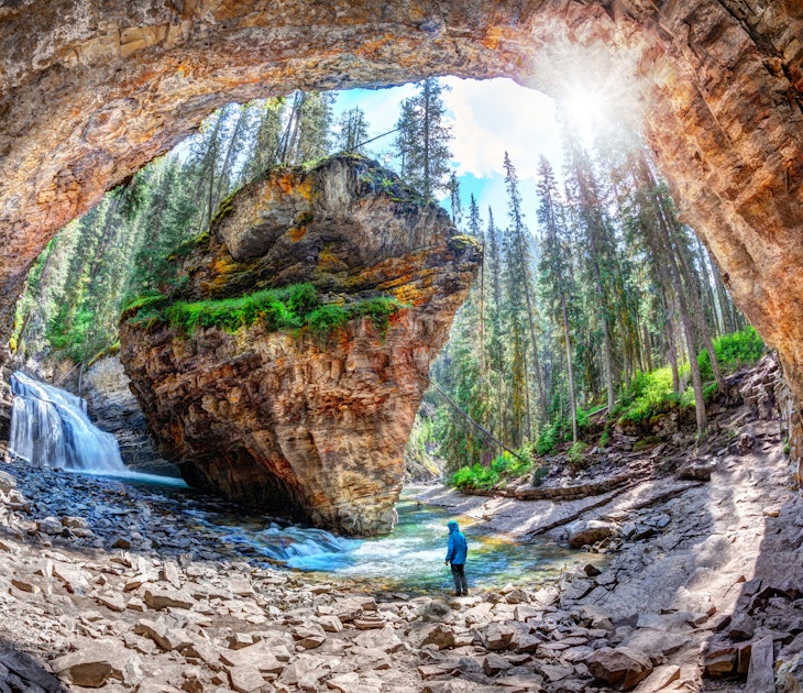 Hiker stands in awe of waterfall and limestone bedrock at a hidden cave in Johnston Canyon at Banff National Park, with sun bursting through the lush forest in the Canadian Rockies.
1015589466