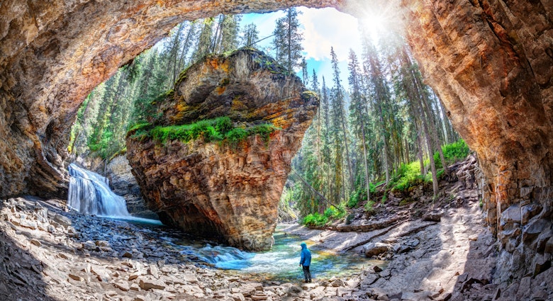 Hiker stands in awe of waterfall and limestone bedrock at a hidden cave in Johnston Canyon at Banff National Park, with sun bursting through the lush forest in the Canadian Rockies.
1015589466