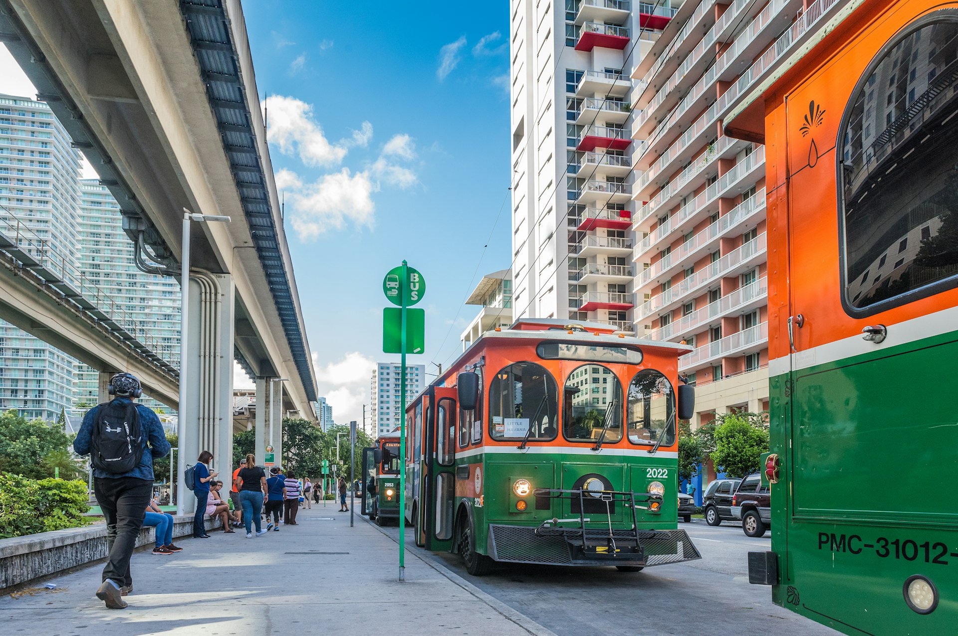 Orange-and-green trolley buses are waiting to pick up passengers at Brickell Trolley Bus Station in Miami