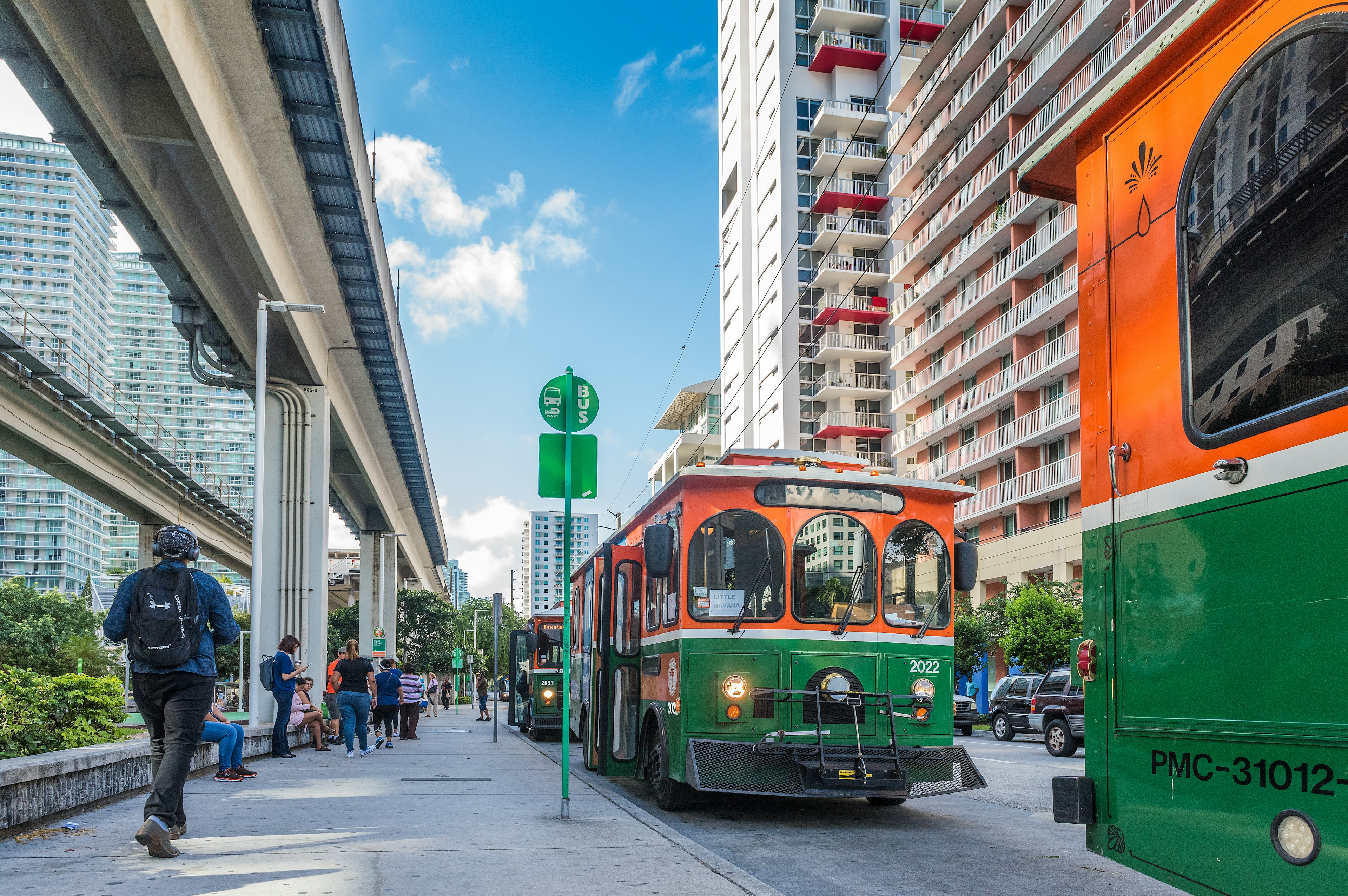 Orange-and-green trolley buses are waiting to pick up passengers at Brickell Trolley Bus Station in Miami