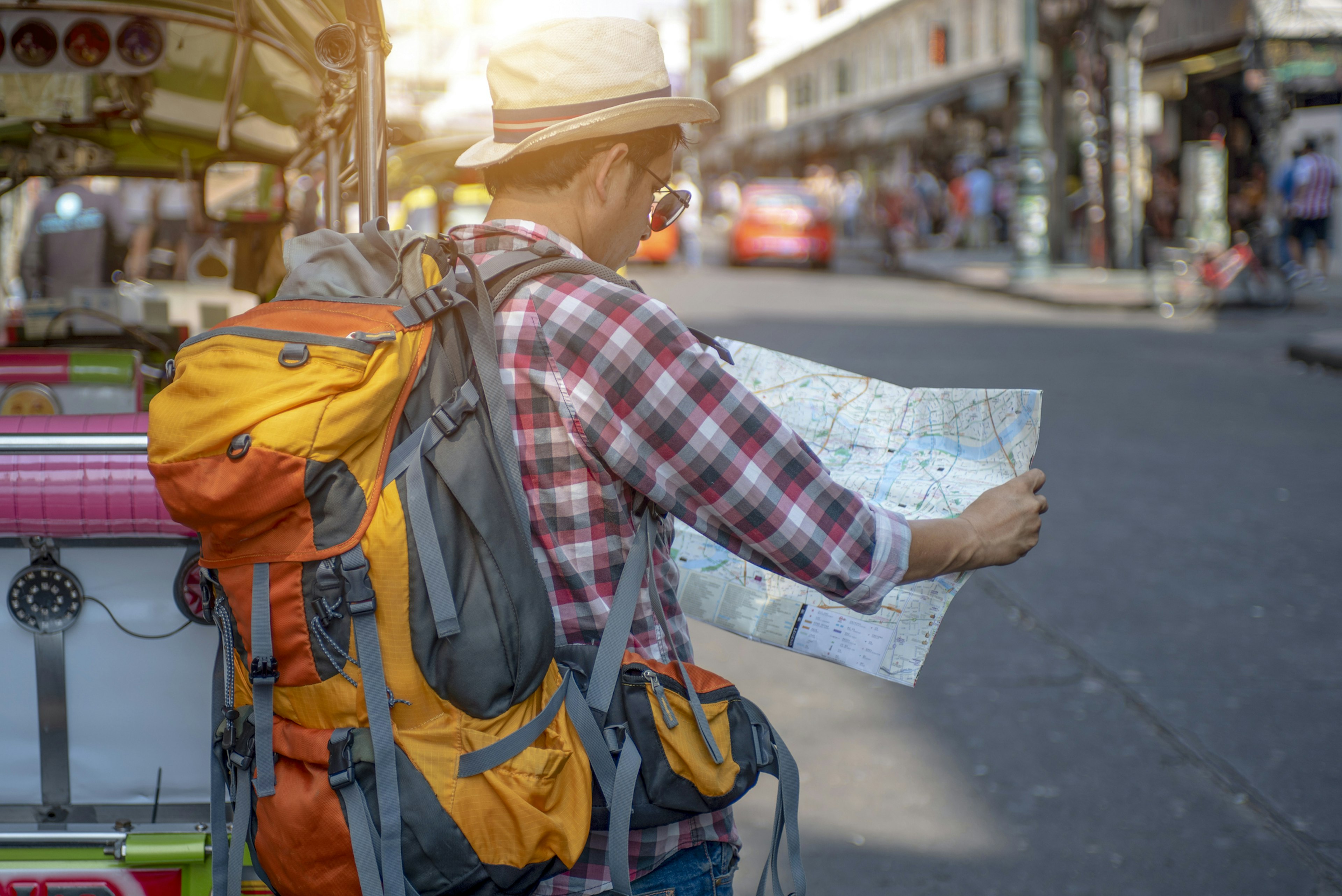 Man wearing a backpack looking at a map on a busy street in Bangkok