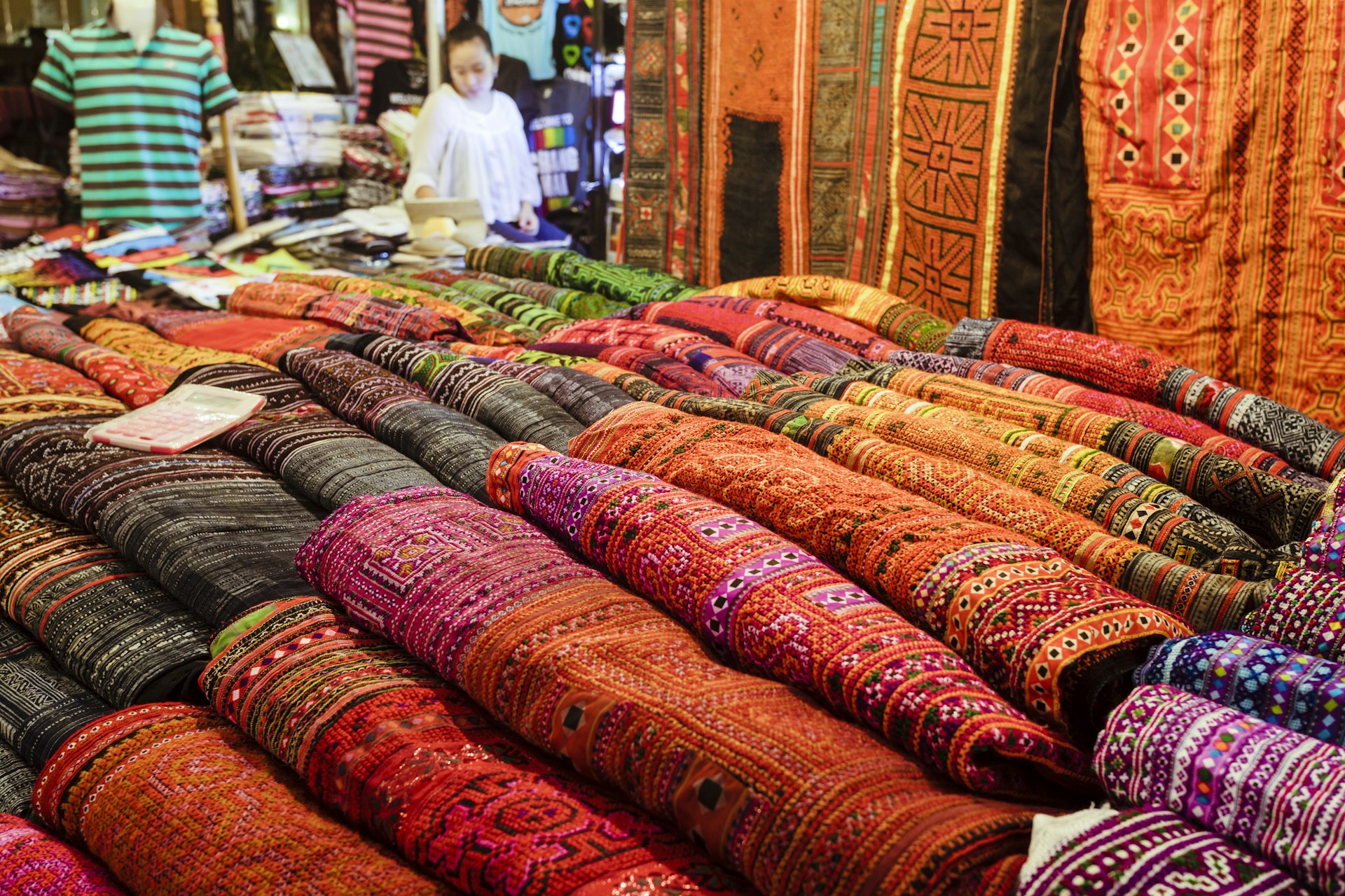 A stall at a night market in Chiang Mai, Thailand, is laid out with brightly colored woven textiles for sale