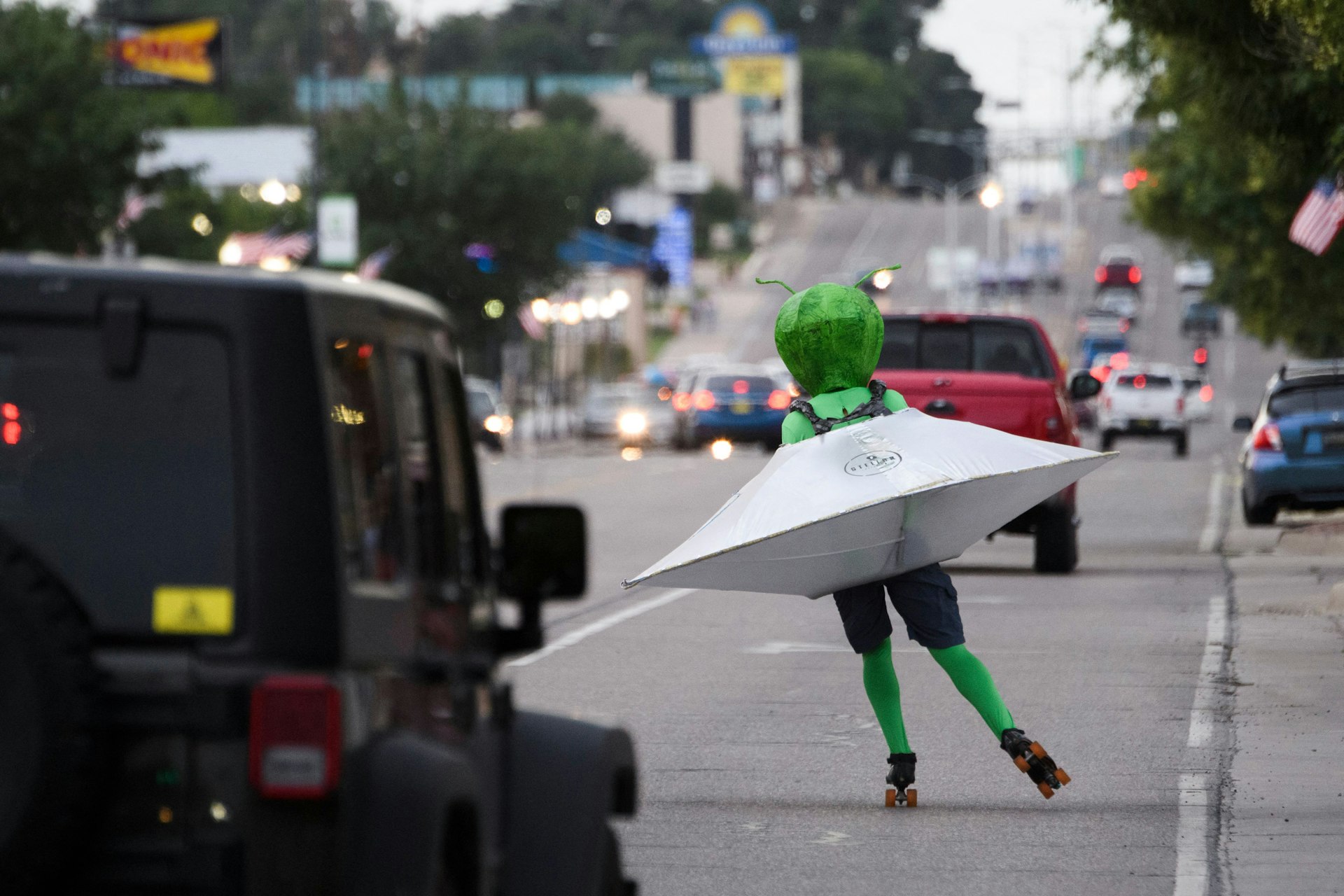 A person wearing an alien costume in a flying saucer roller skates through traffic down Main Street during the UFO Festival on July 2, 2021 in Roswell, New Mexico