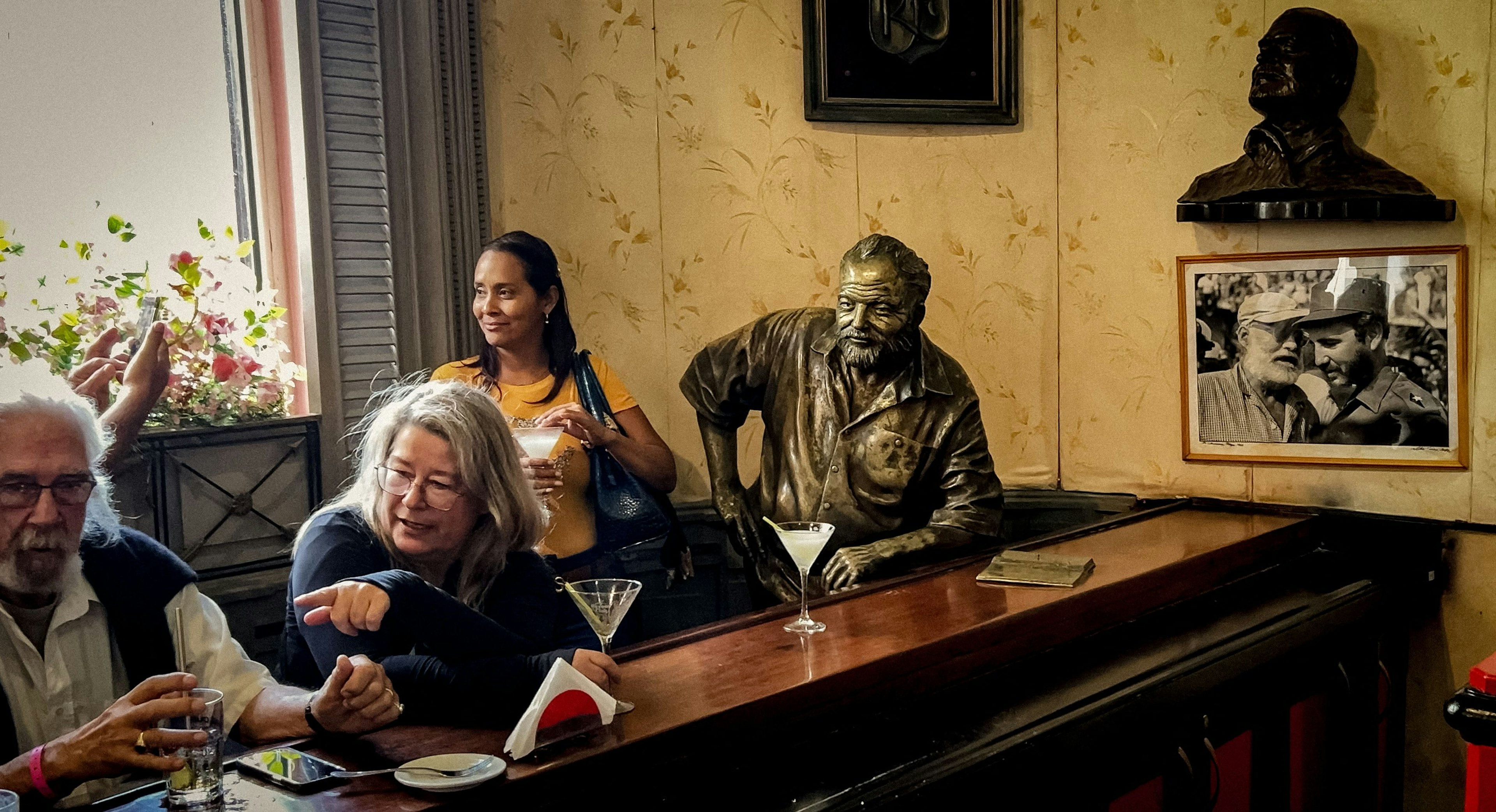 Tourists drink cocktails next to a sculpture of US novelist Ernest Hemingway at El Floridita, Havana, Cuba