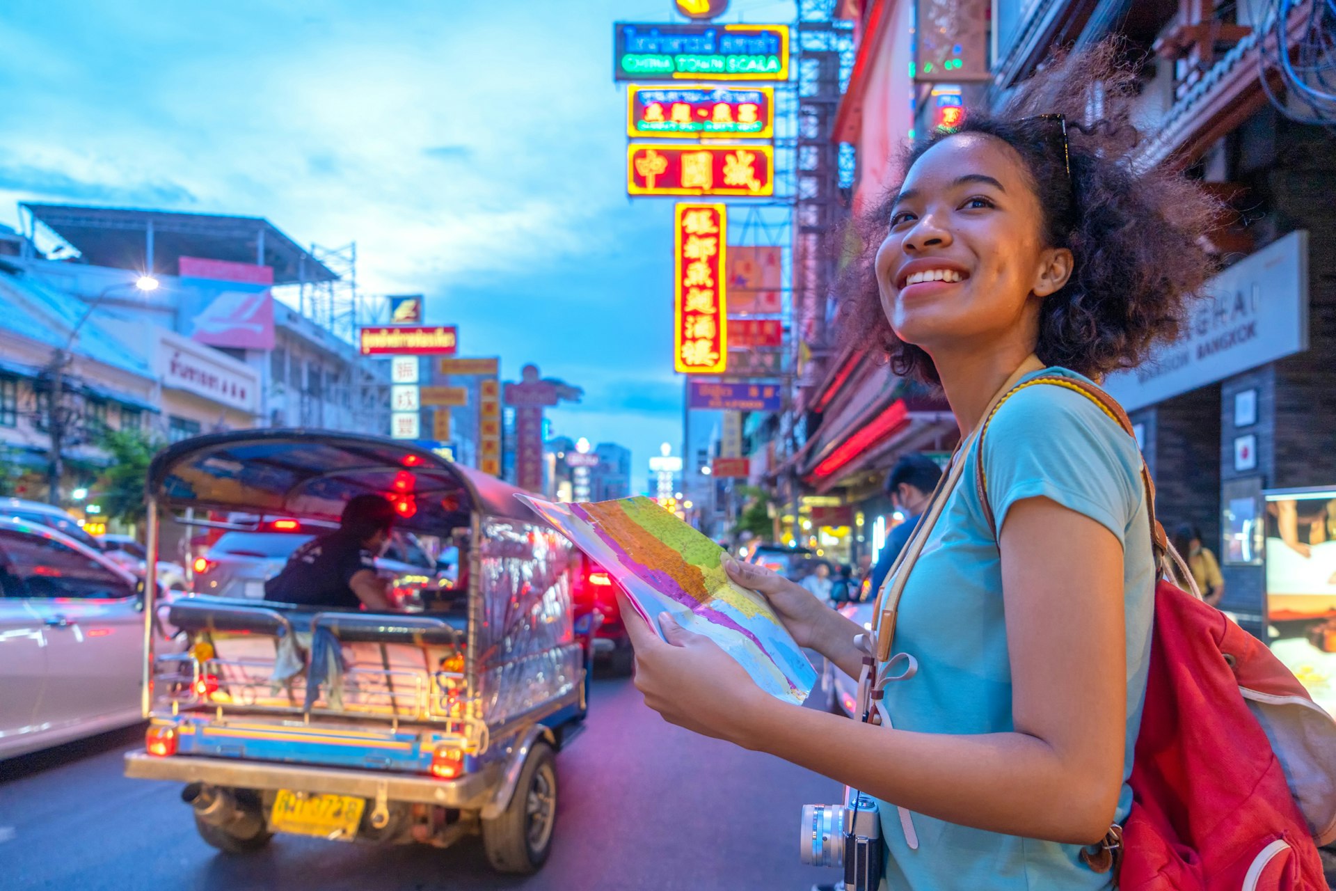 A young woman holding a map and smiling on a busy street in Bangkok, Thailand
