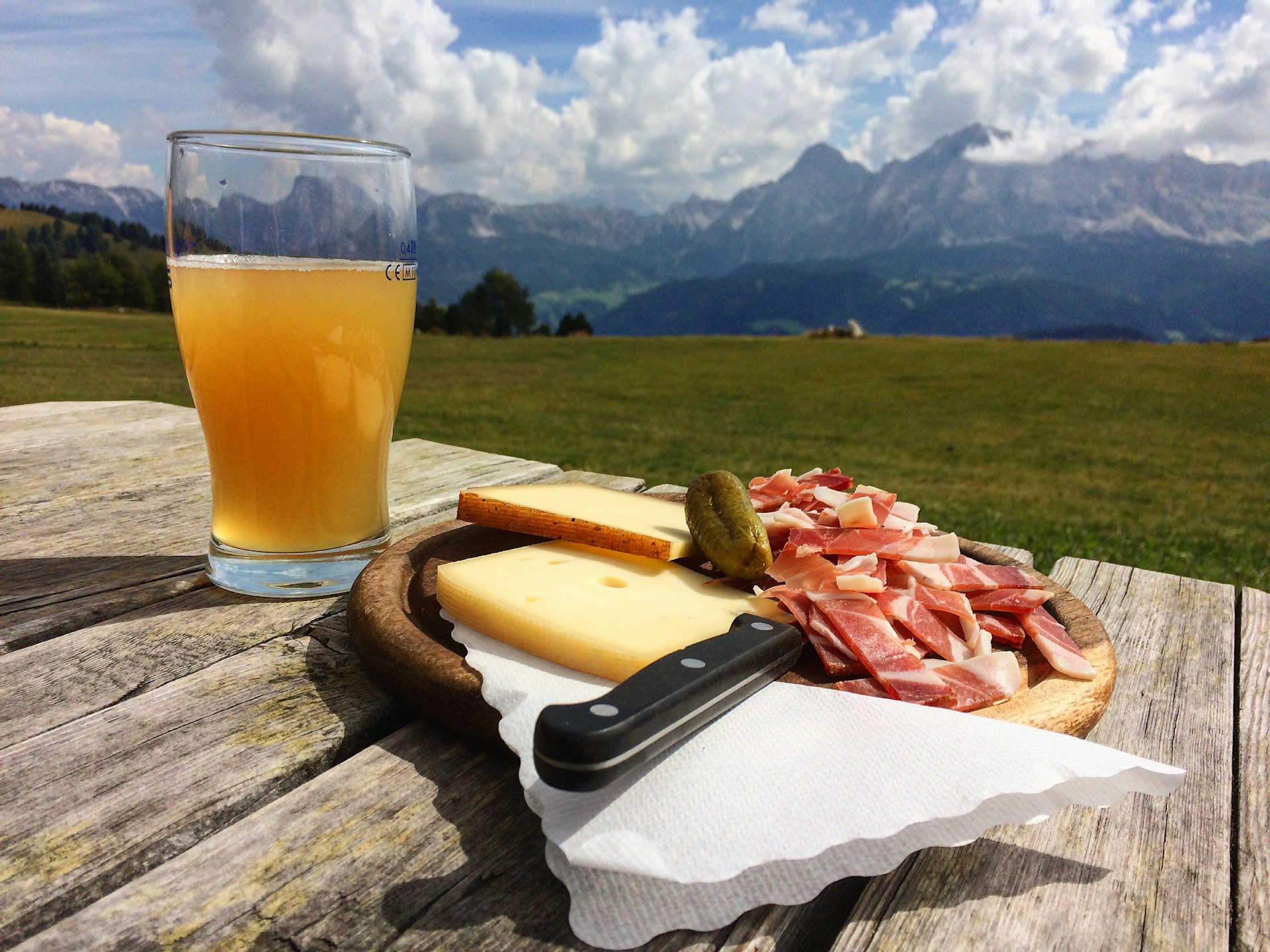 A plate of cheeses with some charcuterie meats on a table next to a beer
