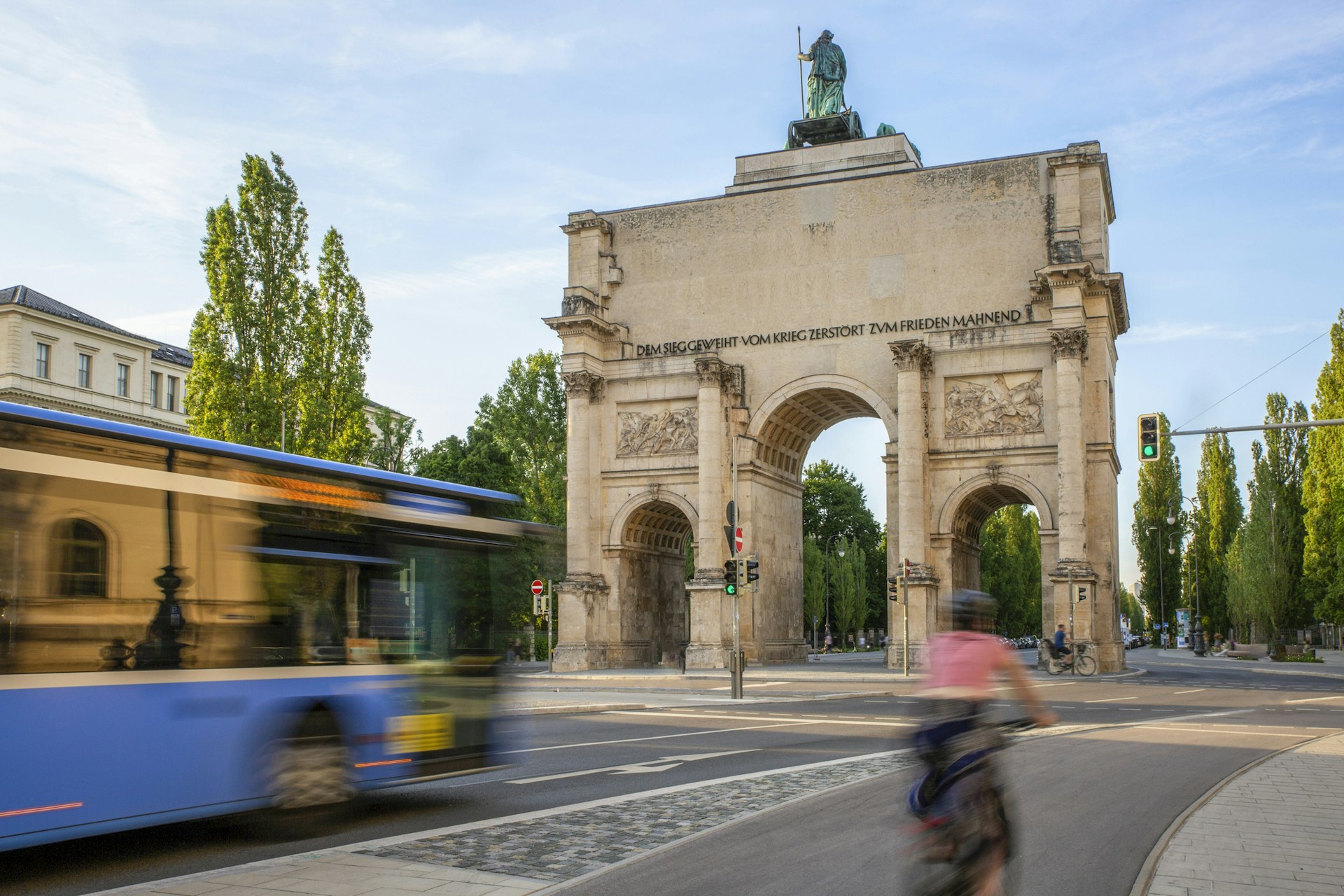 A cyclist and bus in blurred motion as they speed past an ornamental arch in a city