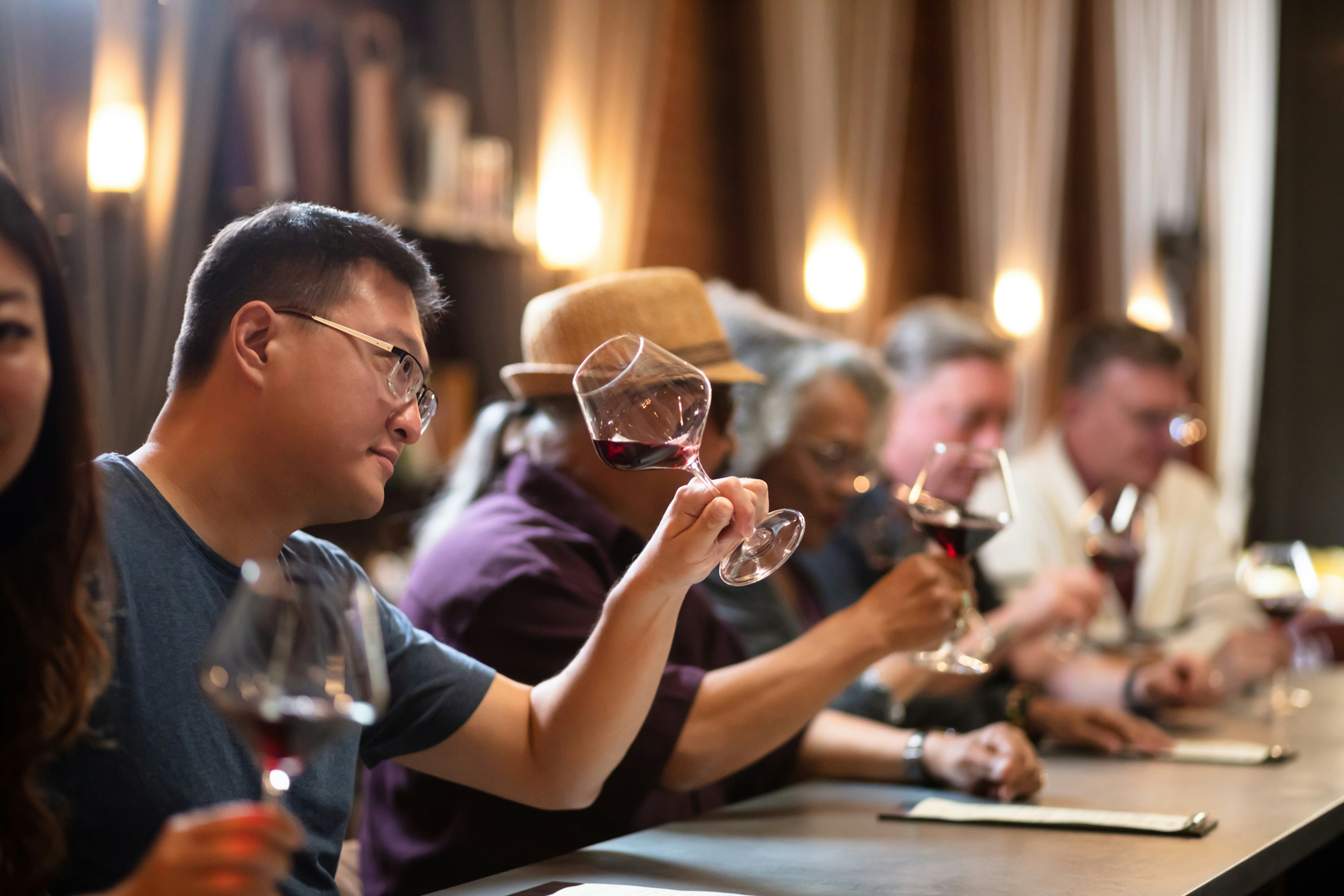 People at a bar in a wine tasting room inspect the wine in their glasses