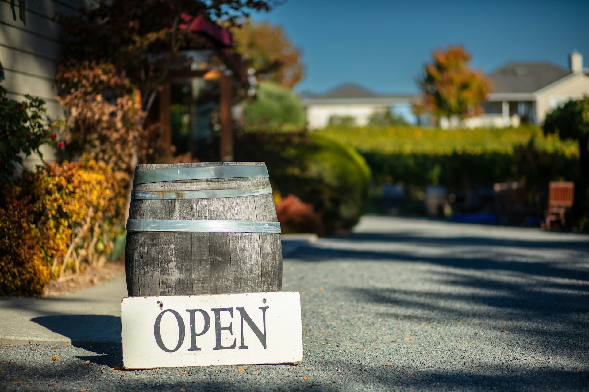 Decorative barrel of wine with an "Open" sign sitting in sunlight next to a vineyard