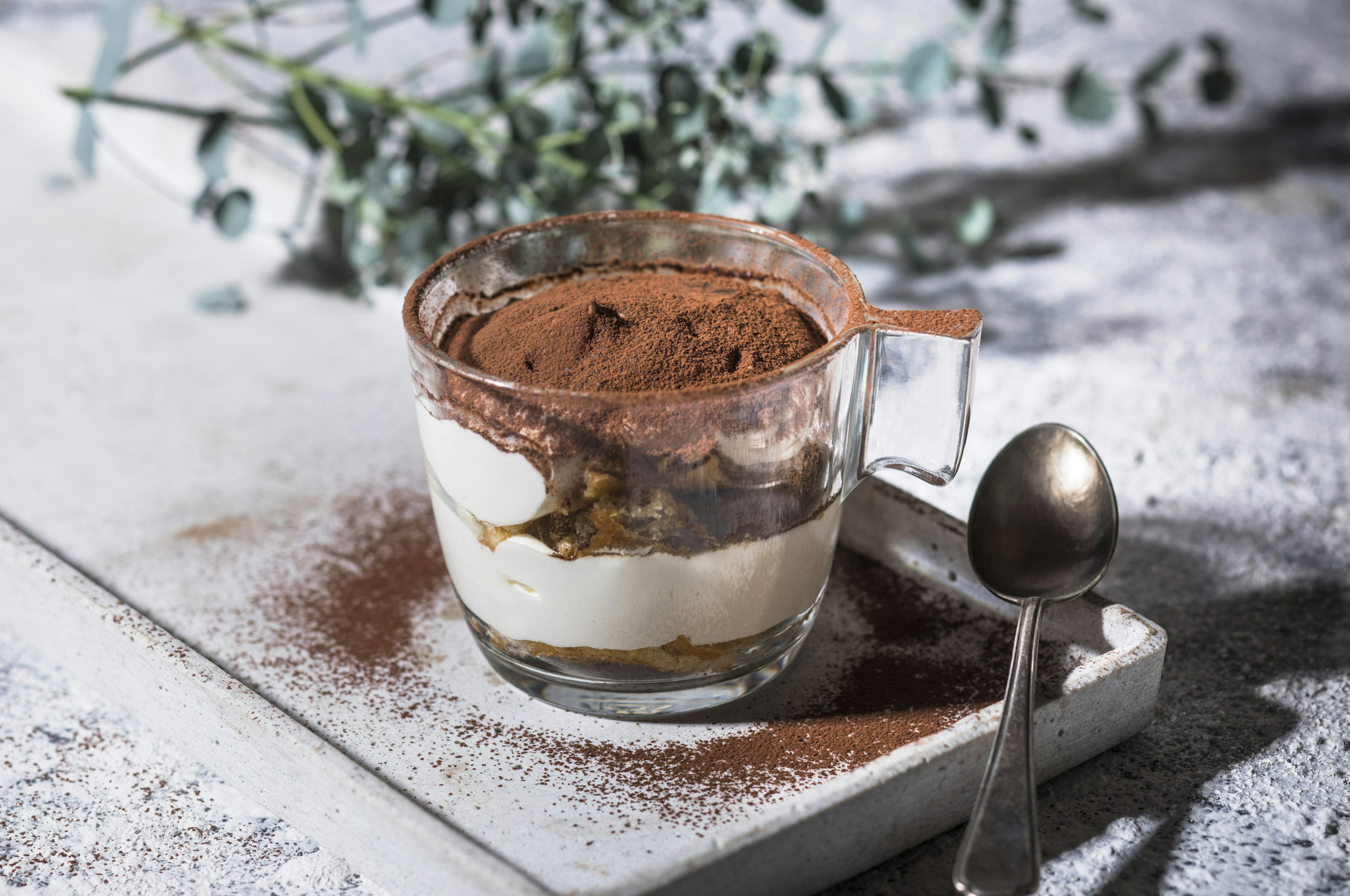 A brown-colored pudding in a glass mug with a spoon on a tray