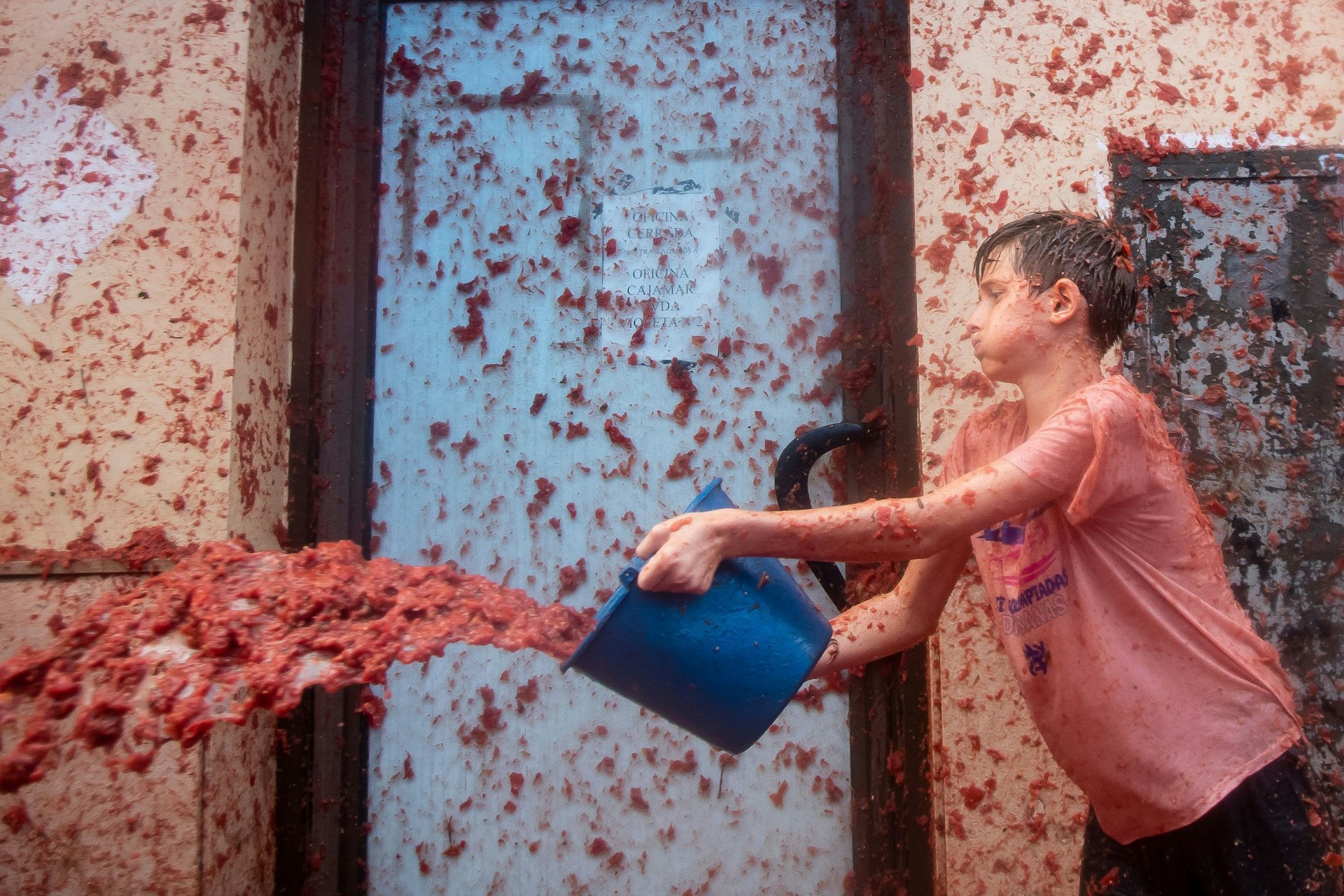 A boy used a bucket to hurl crushed tomatoes during La Tomatina tomato-throwing festival, Buñol, Spain