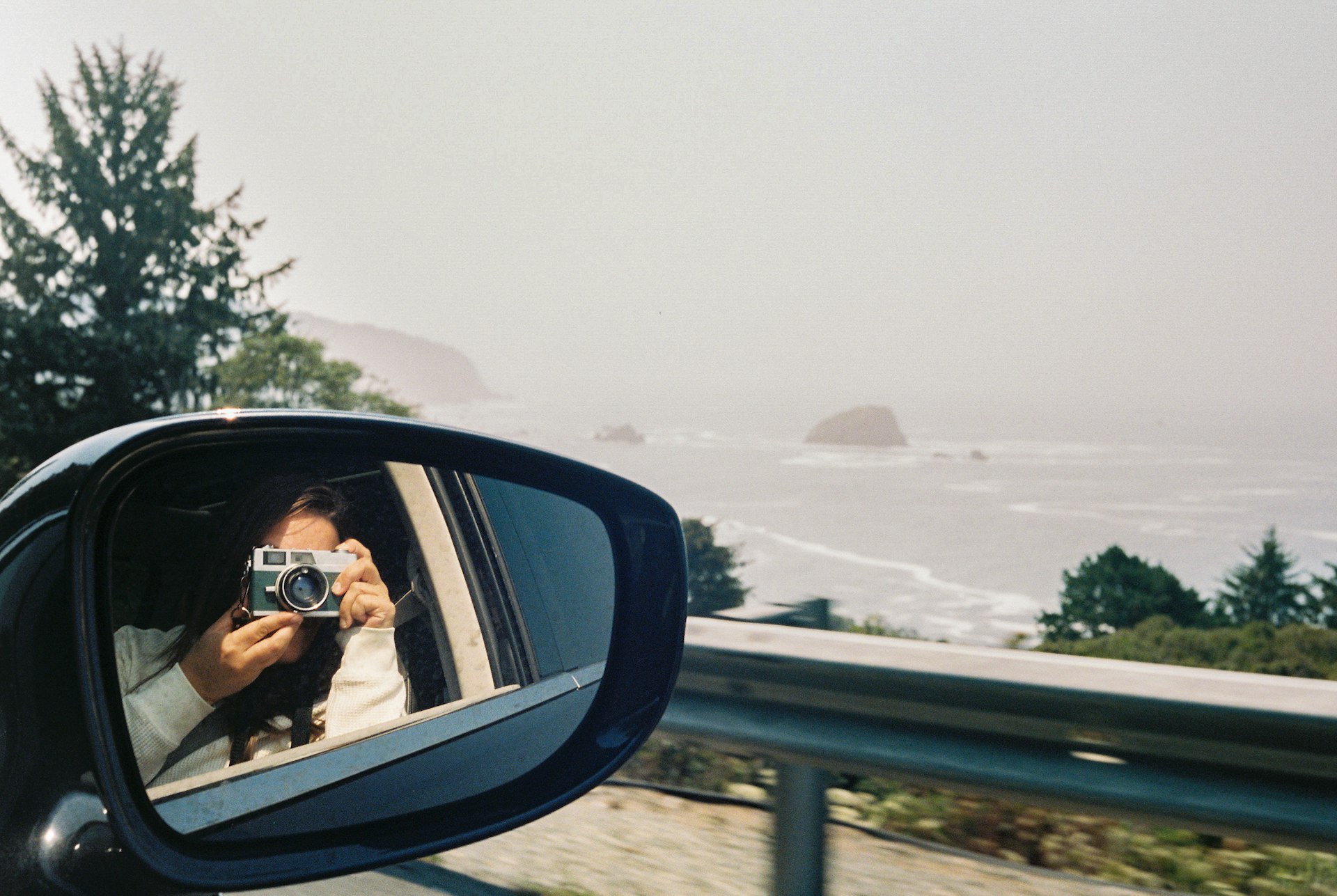 Woman taking a mirror selfie of the coast in a car on a road in Seaside, Oregon, USA