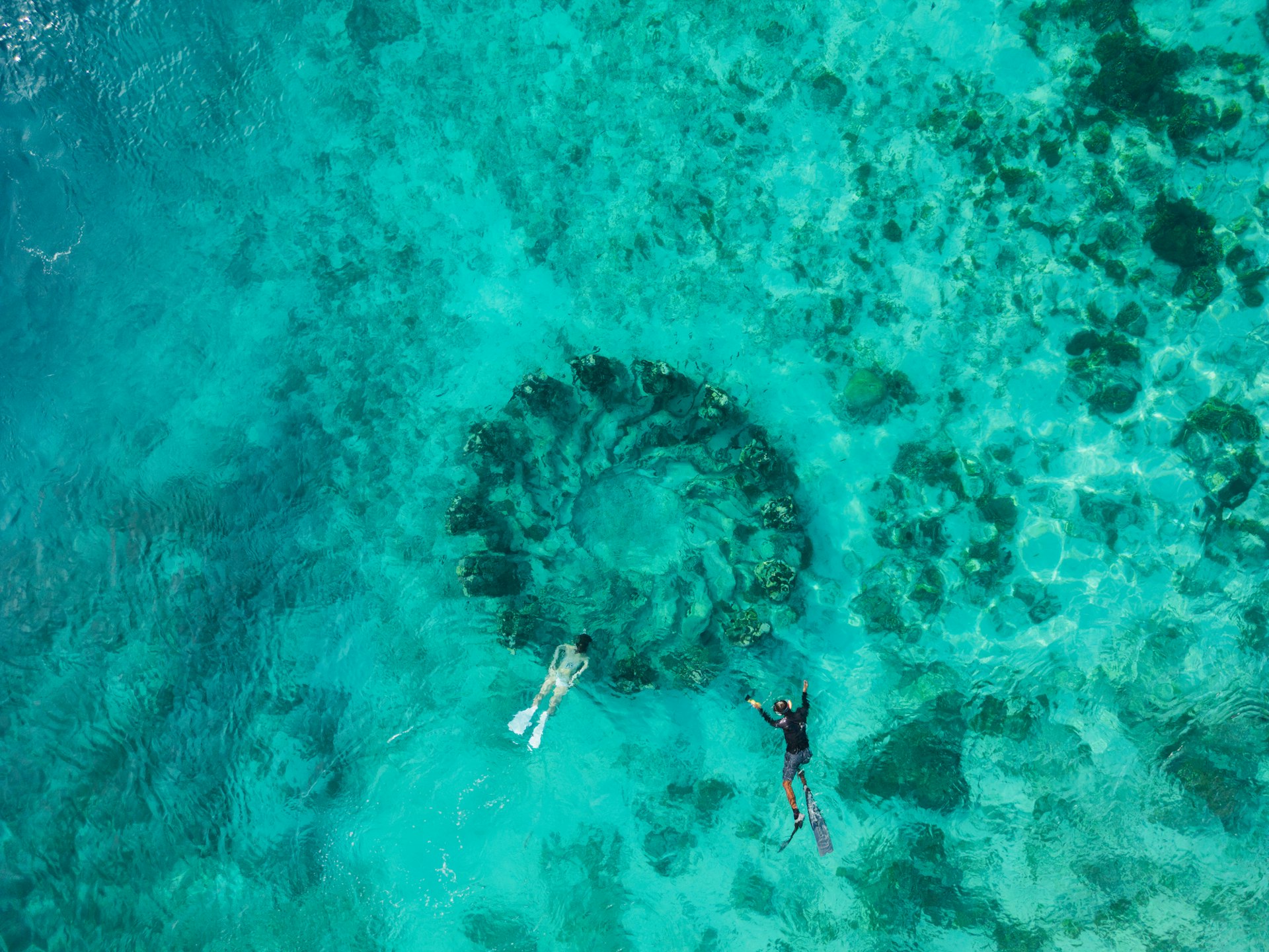 A couple snorkel in clear turquoise waters above an underwater sculpture of figures standing in a circle