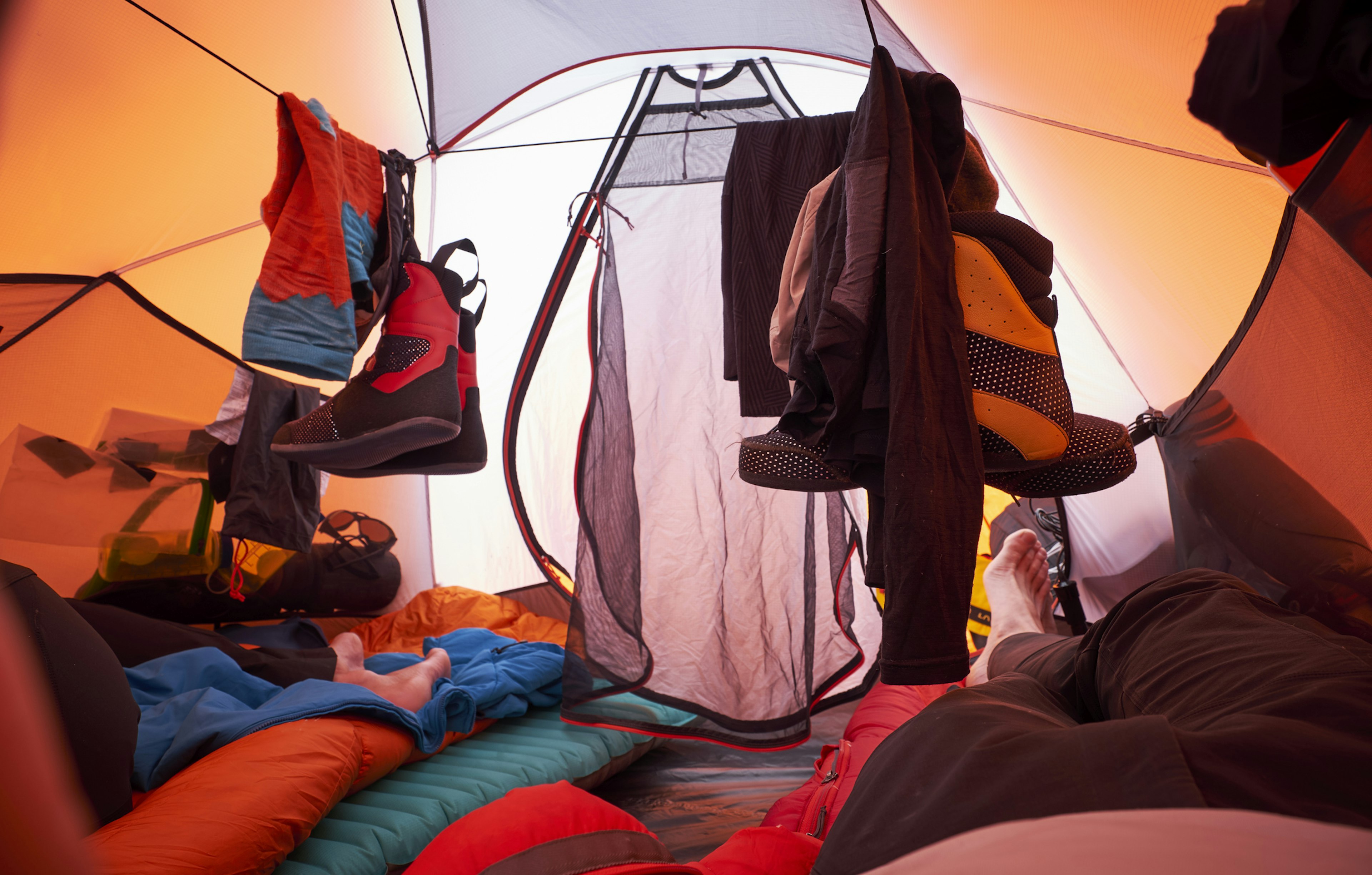 Climbing gear hangs to dry in the tent during a climb on Denali, the climbers are resting on their sleeping bags.