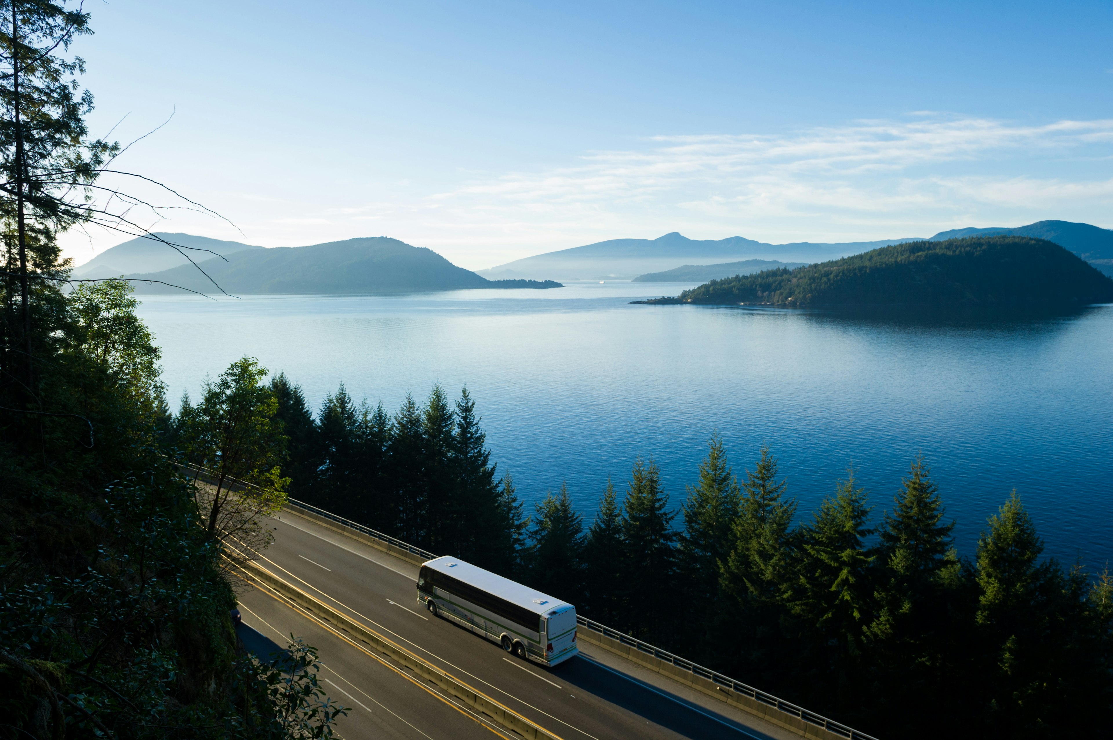 A bus drives along a coastal highway with views out to forest-covered islands