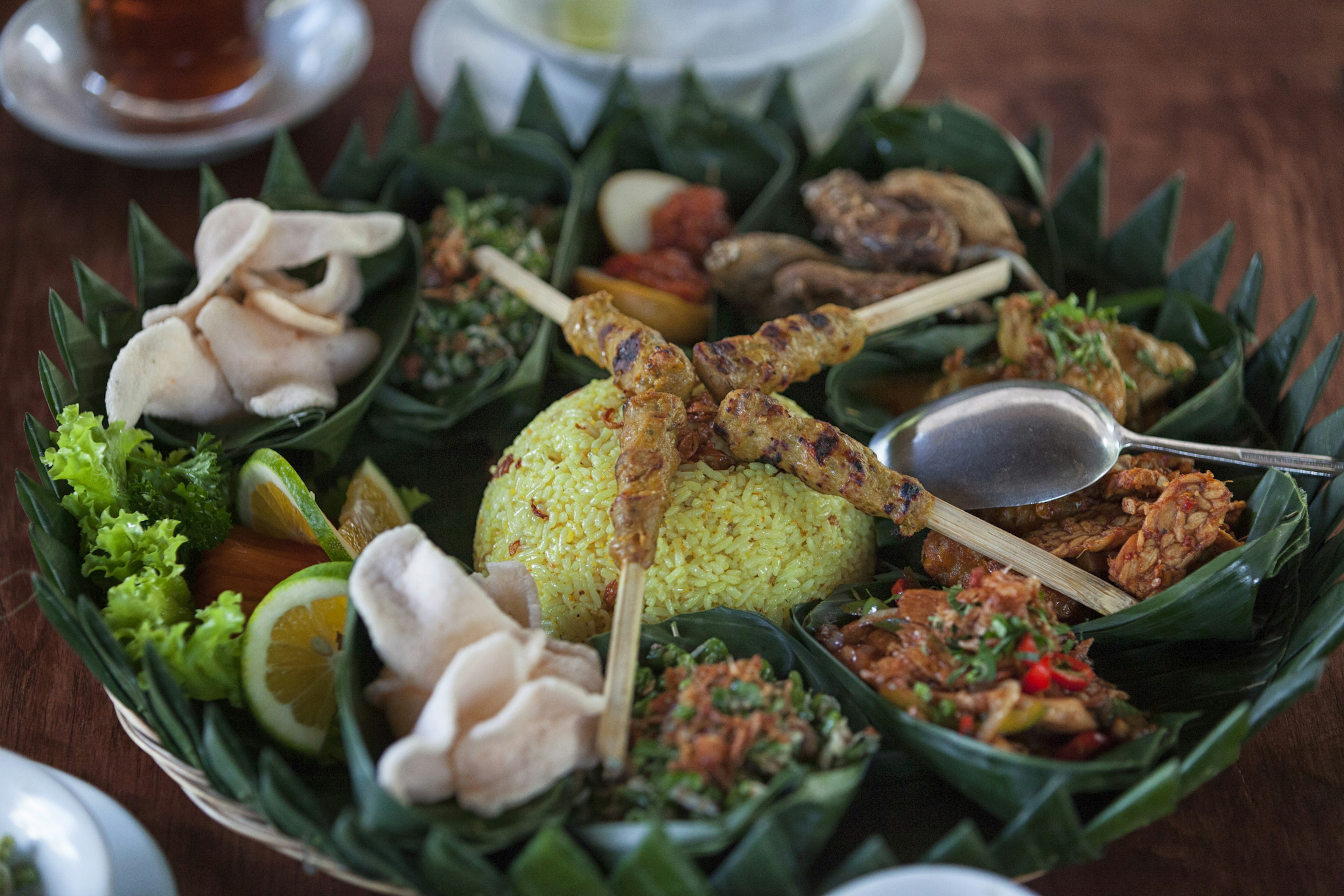 A series of small curries and savories places around a mound of rice with meat skewers on top