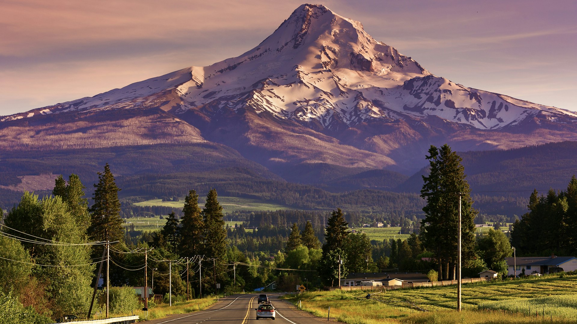 Route 35 leading to snow-covered Mount Hood, Oregon, at sunset, with two cars on road.