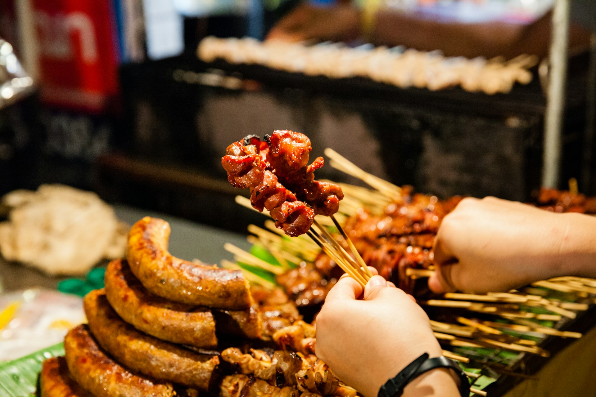Hands holding meat skewers at a market stall in Chiang Mai, Thailand