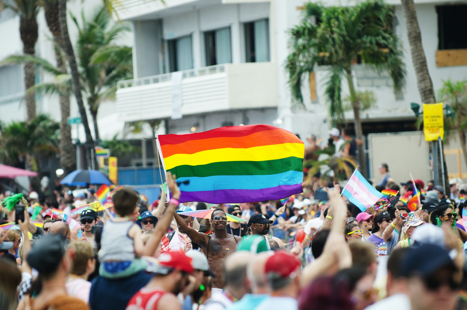 A huge crowd of people waving Pride flags cheer participants walking in the annual Miami Beach Pride Parade on Ocean Drive in South Beach.