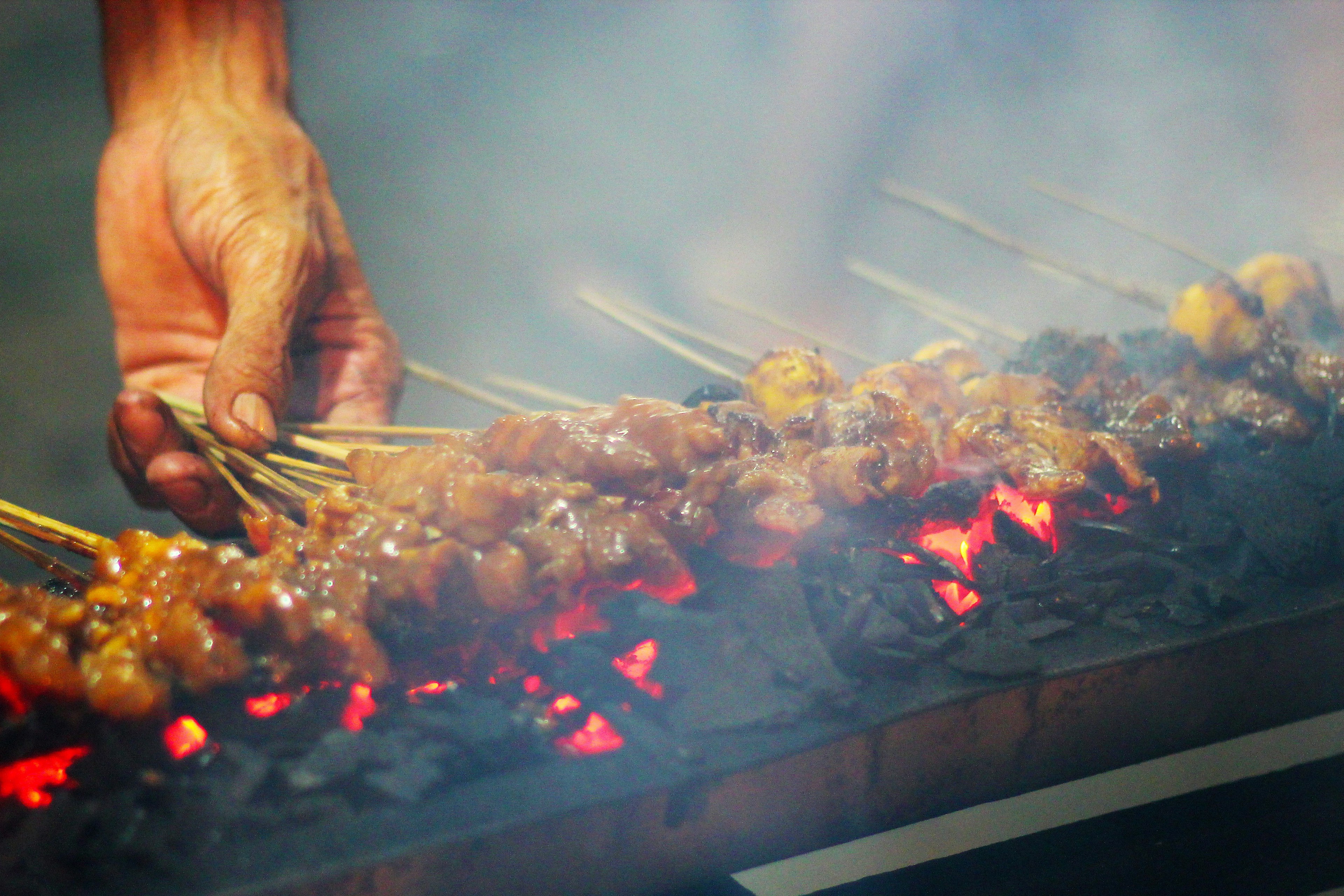 A market seller grilling meat satay on a charcoal burner on the streets of Jakarta, Indonesia.