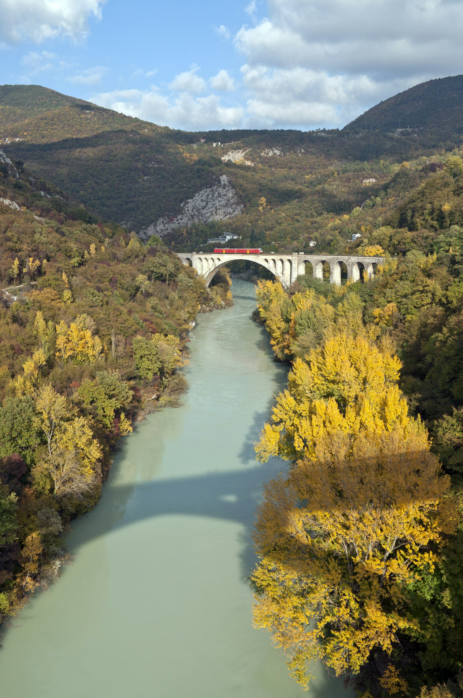 A train crosses a stone bridge over a fast-flowing river