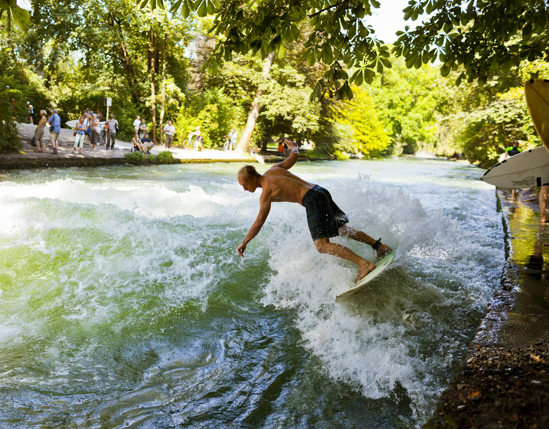  Man surfing with other people watching at the Eisbach river in Munich Germany. 
