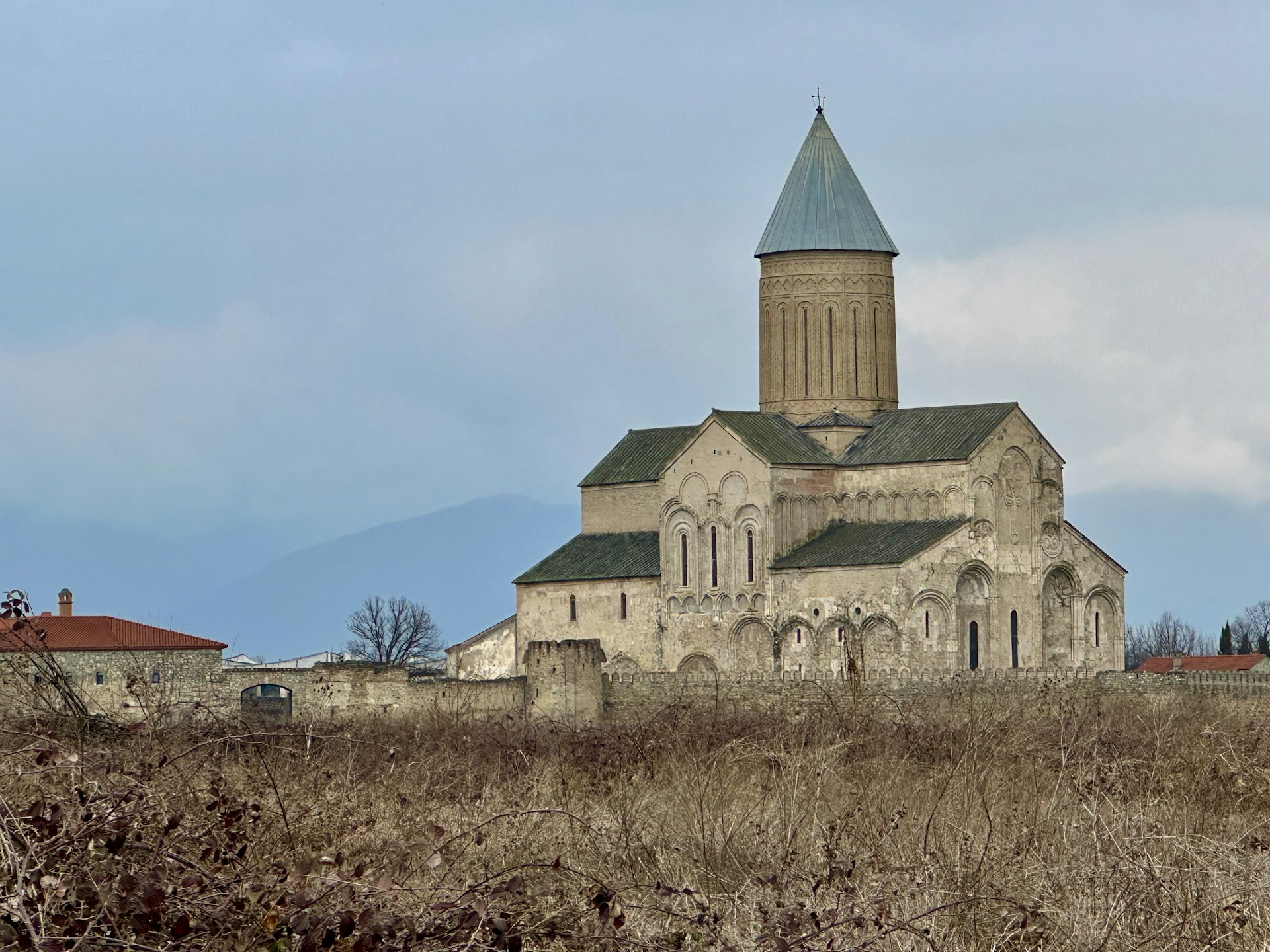 A large stone cathedral stands in front of shady mountains. 