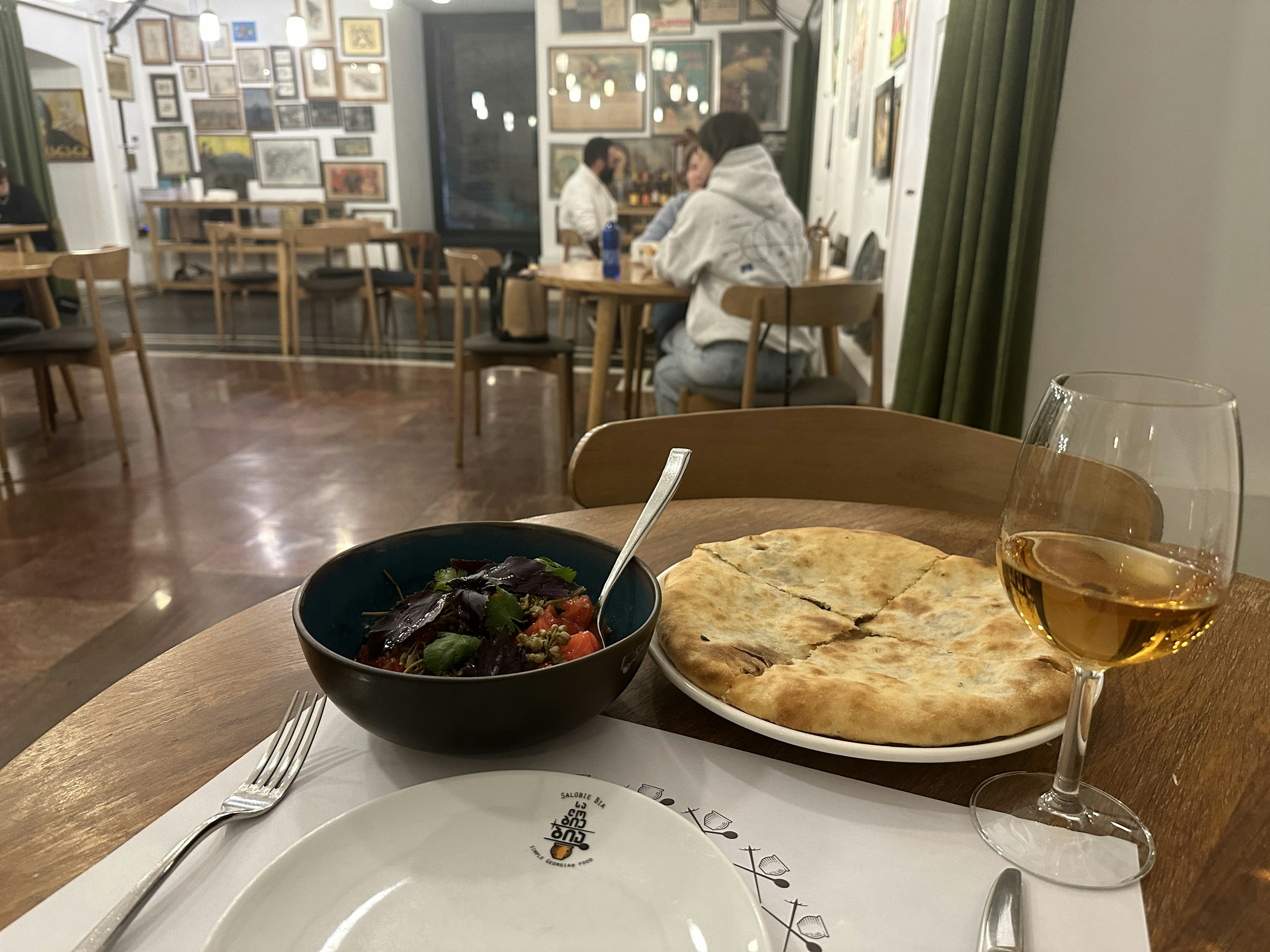 A table with a glass of wine, bread, and tomato salad.