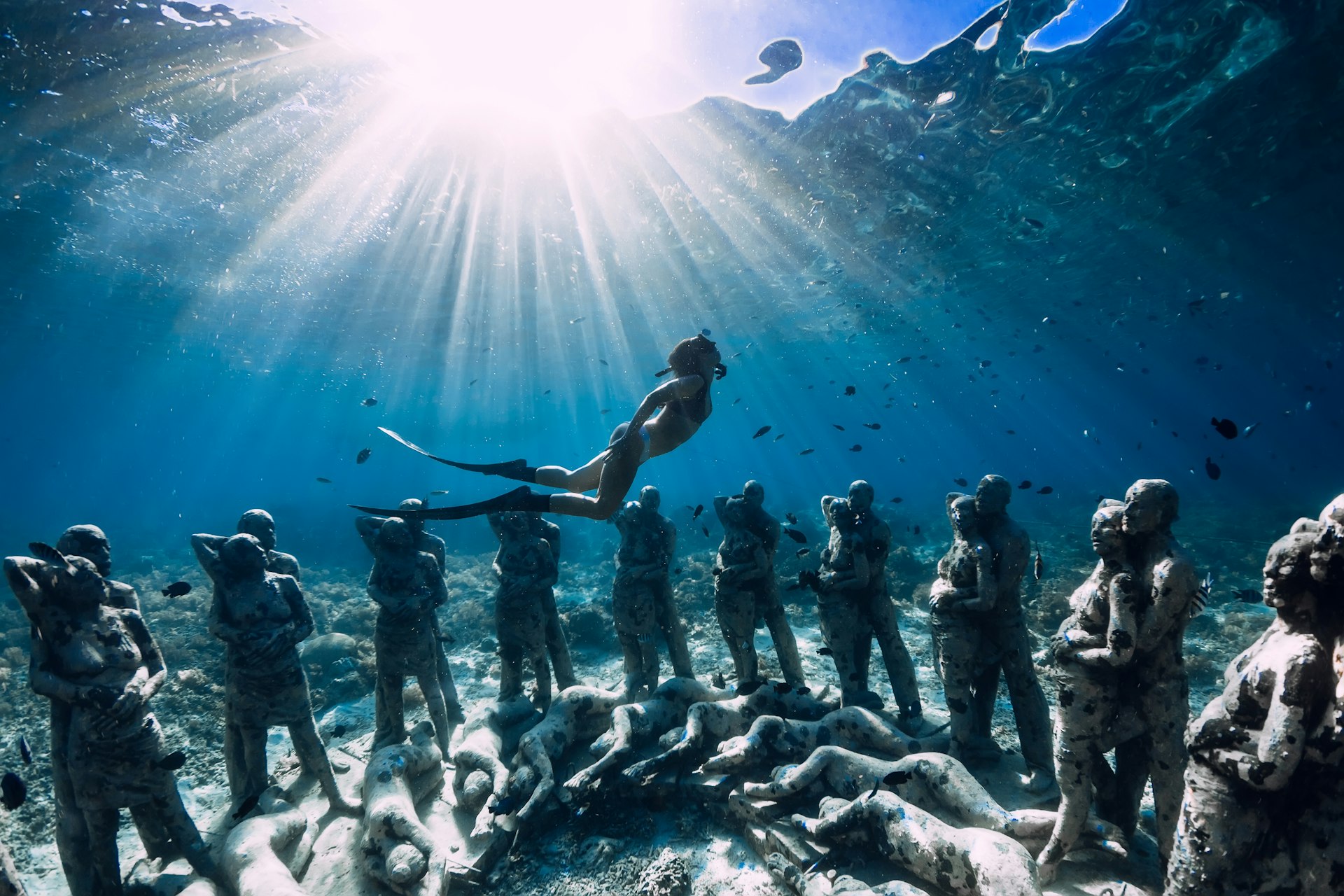  Woman freediver with fins dive near underwater statues. Underwater tourism in the ocean.